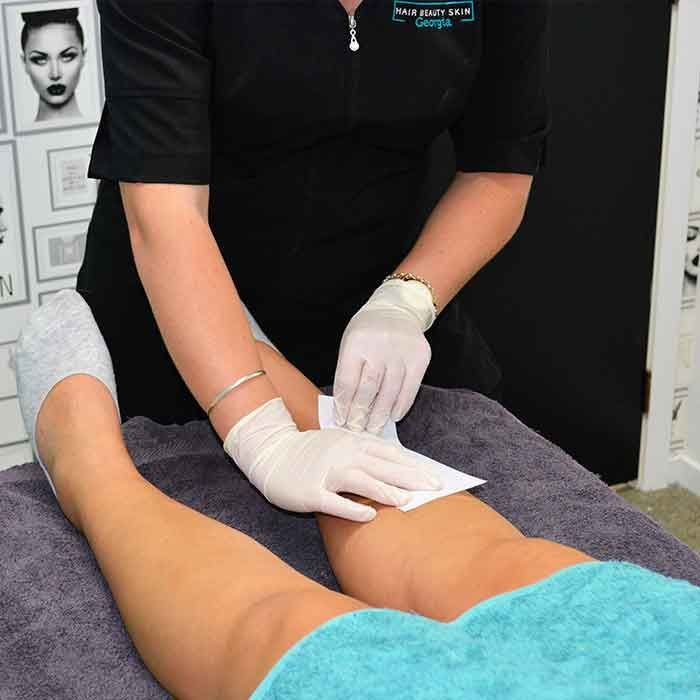 A woman wearing white gloves is waxing a woman 's leg