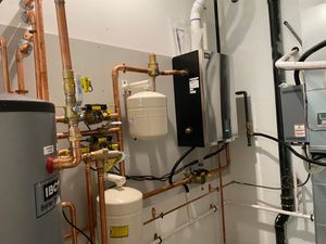 Boiler room with copper pipes, white tanks, and gray HVAC equipment along a wall.