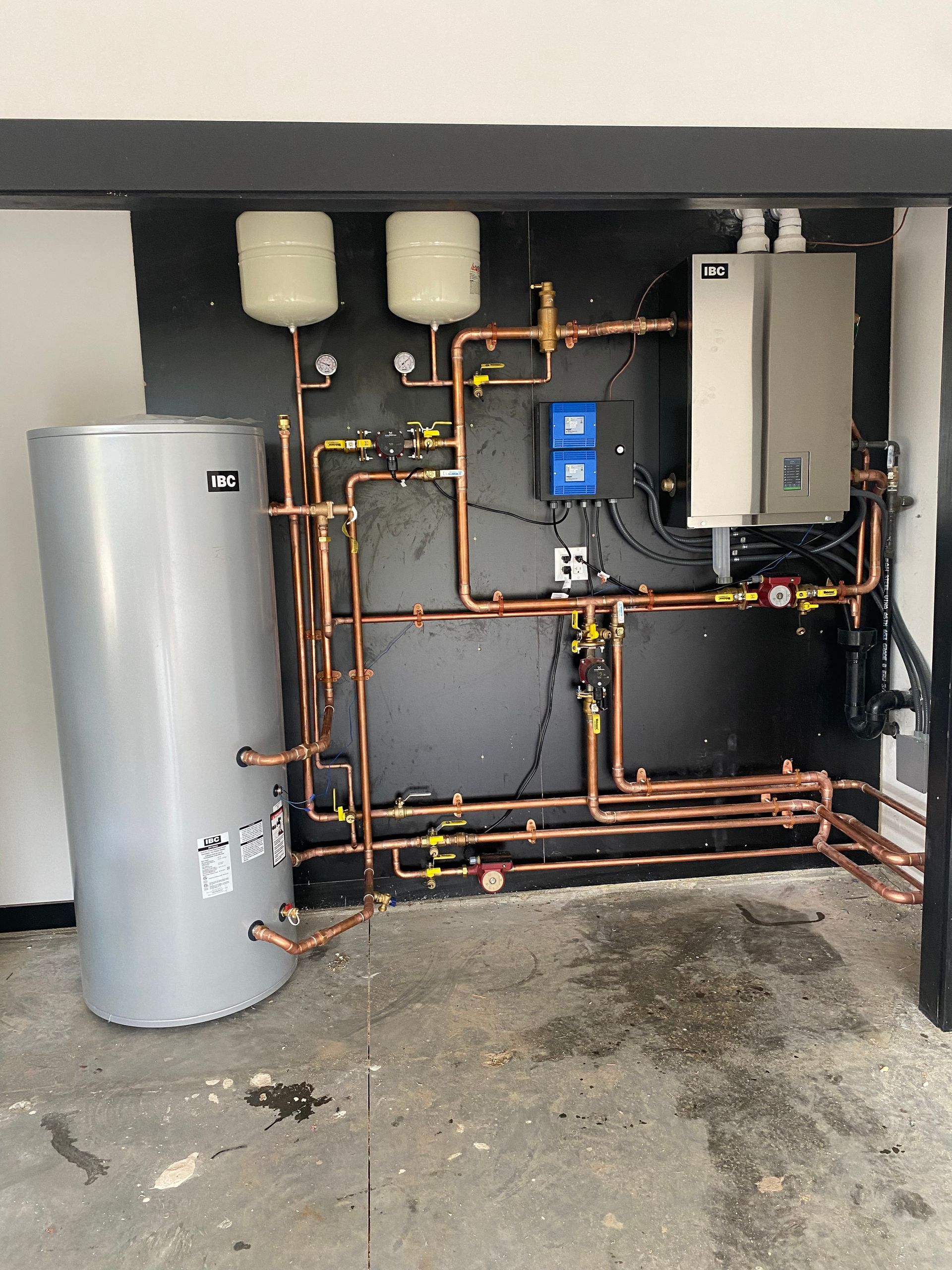 Water heater and boiler room with copper piping, tanks, and control units in a utility space.