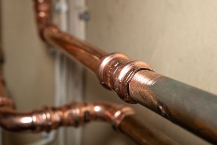 Close-up of copper pipes with shiny joints against a beige wall.