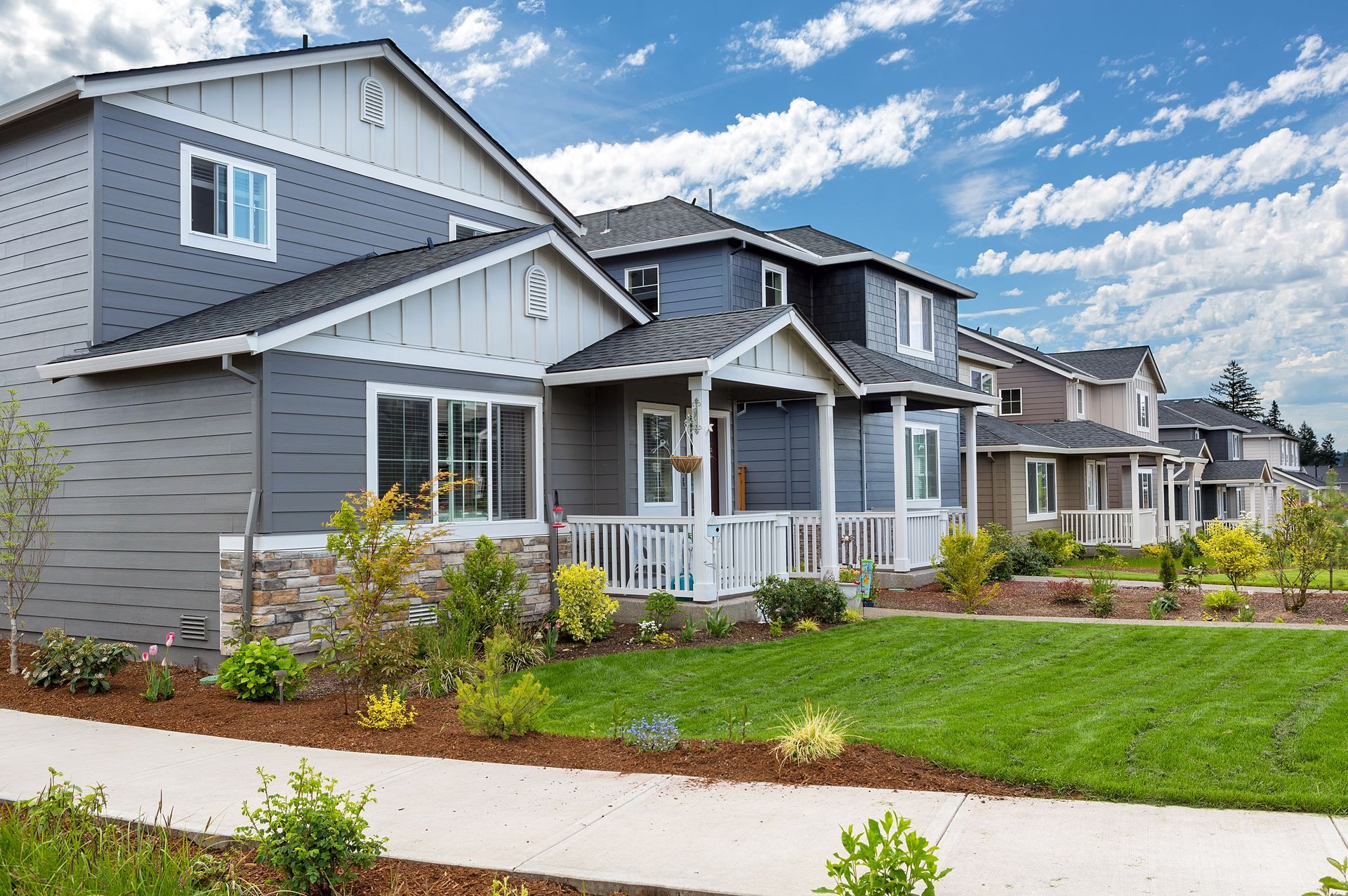 A row of modern, two-story homes with dark blue siding and stone accents under a bright, cloudy blue sky. A row of modern, two-story homes with dark blue siding and stone accents under a bright, cloudy blue sky.