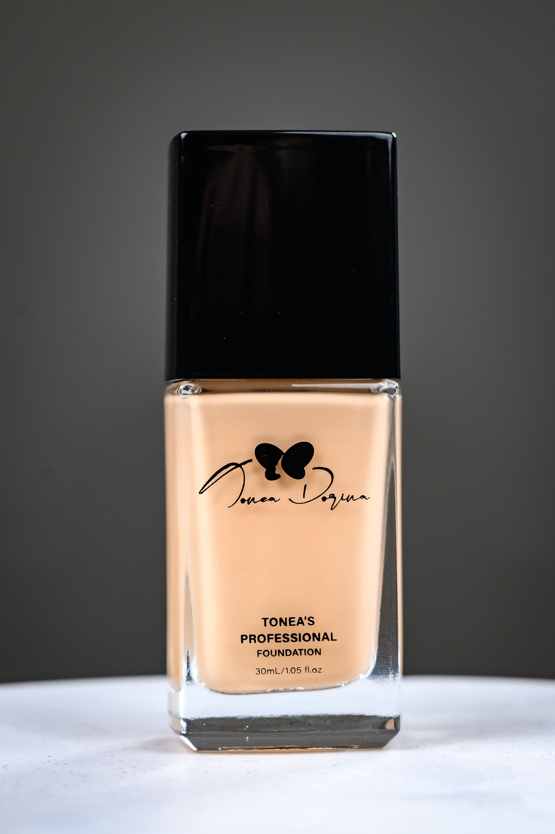 Beigefarbene Make-up-Flasche mit schwarzem Deckel auf weißem Untergrund vor grauem Hintergrund