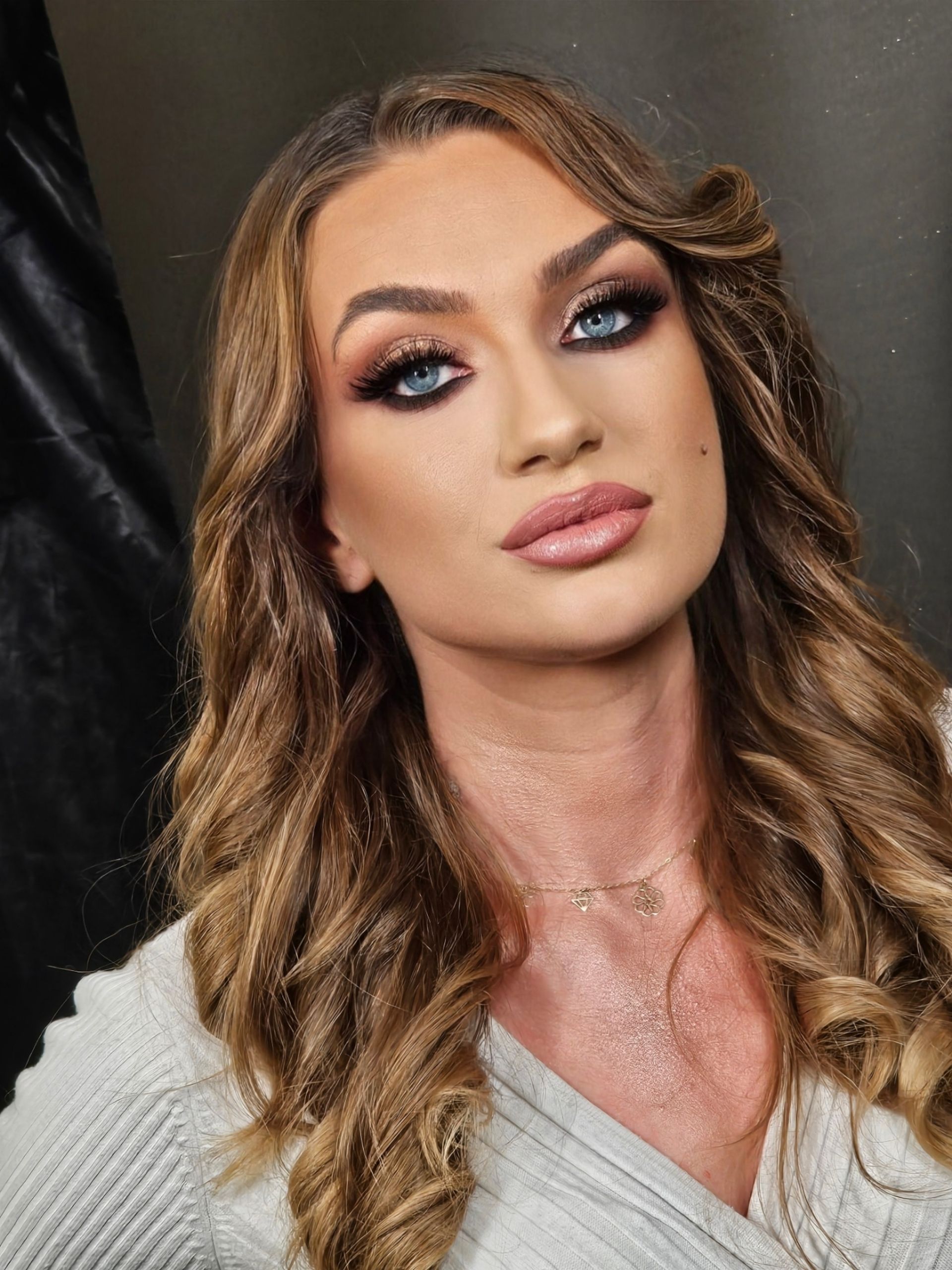 Frau mit langem, welligem braunem Haar und dramatischem Make-up; posiert mit Blick nach vorne.
