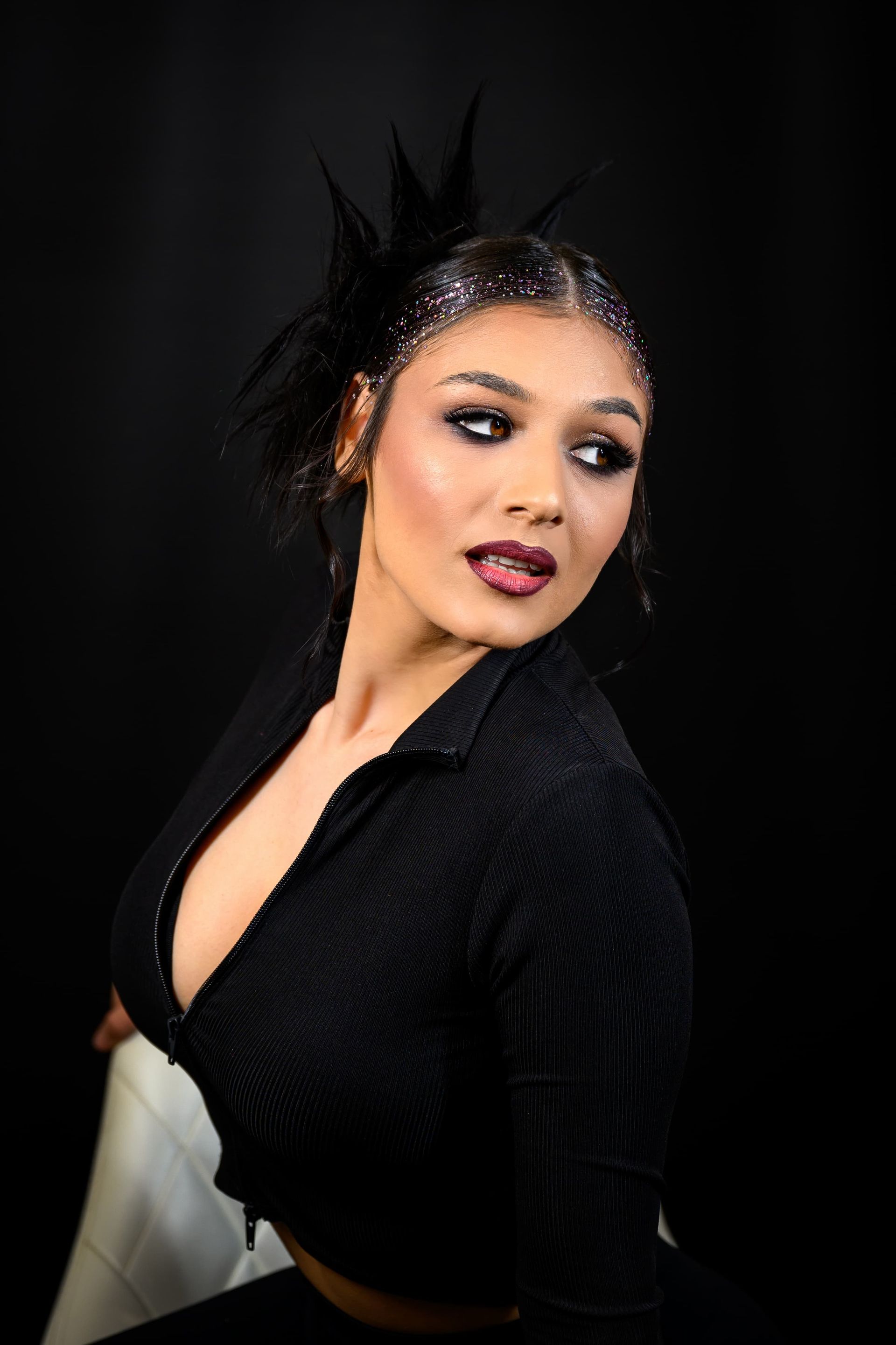 Frau in schwarzem Outfit mit dunklem Augen-Make-up, die über ihre Schulter blickt.