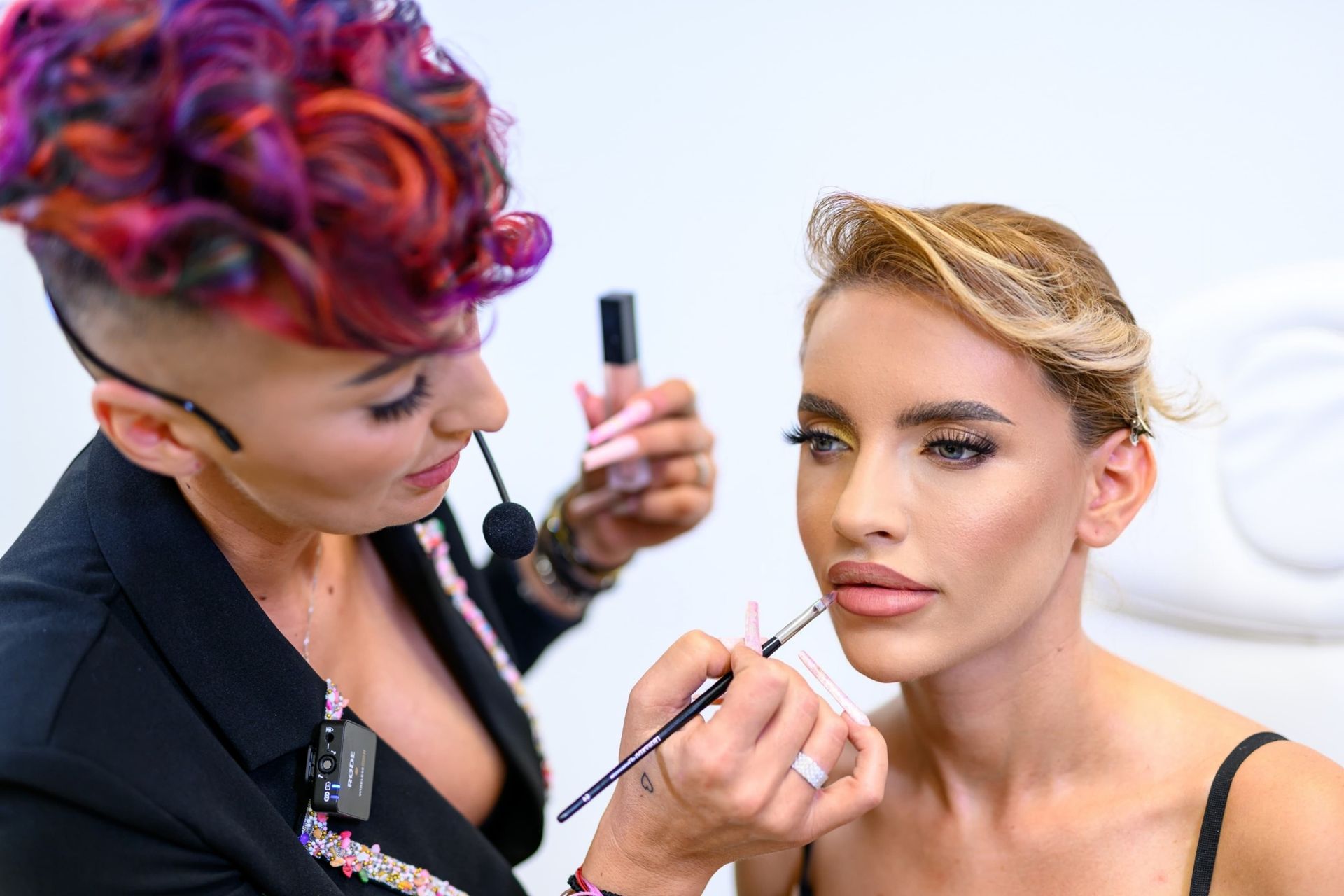 Maskenbildnerin trägt Lipgloss auf die Lippen eines Models auf. Helle Beleuchtung.