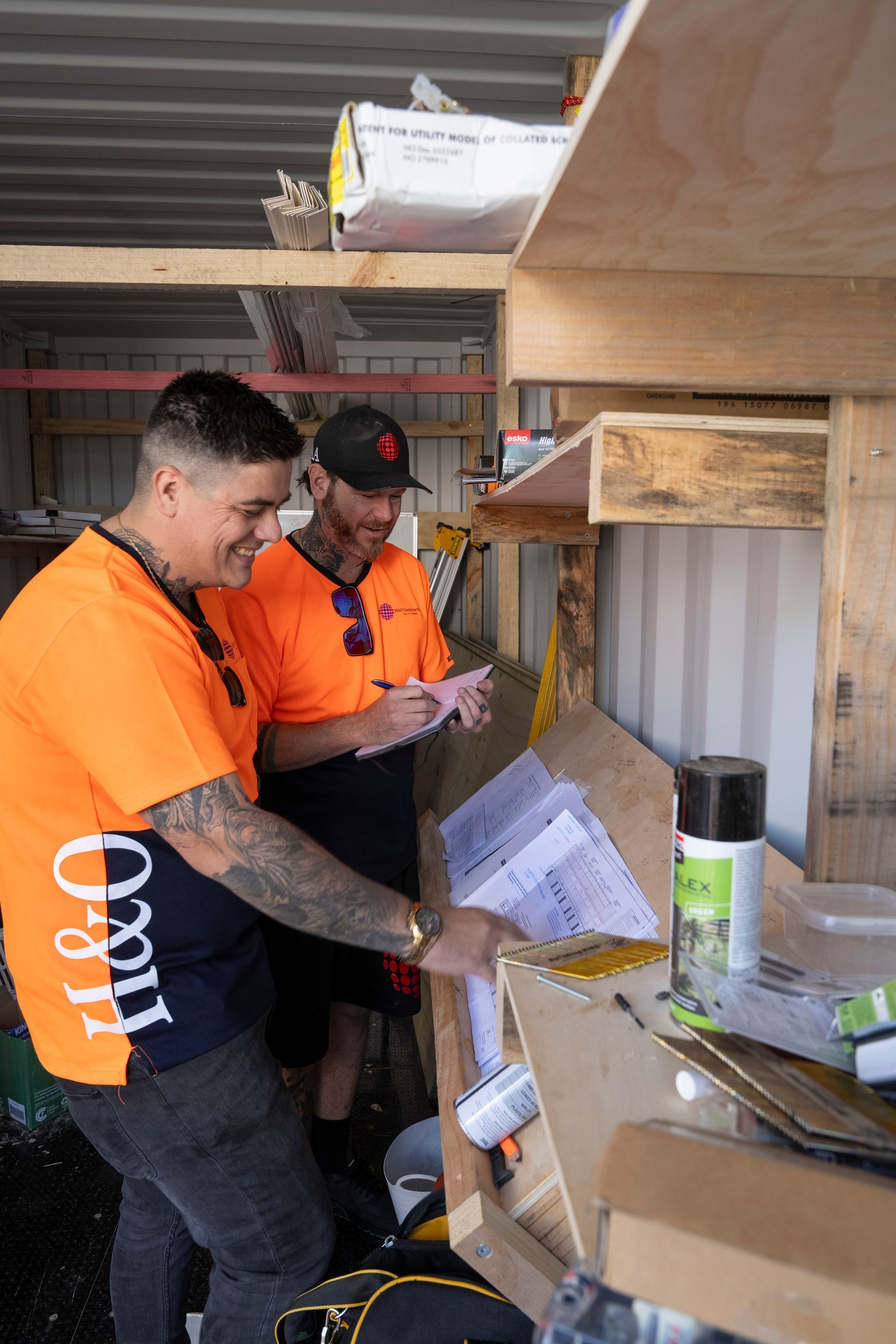 Two men are standing in a shed looking at papers.