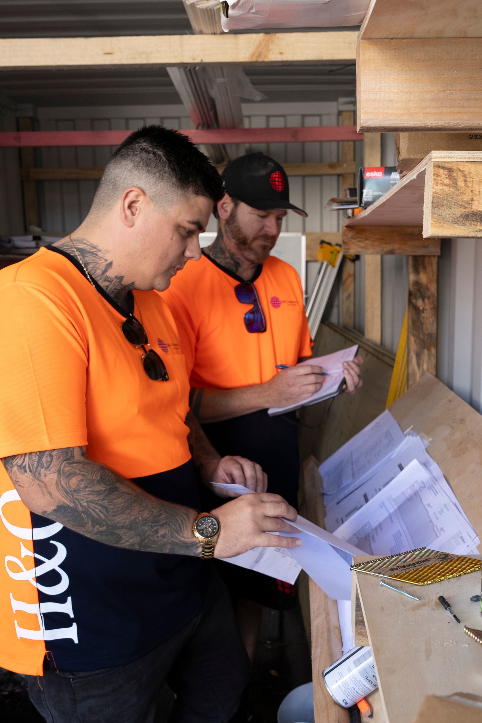 Two men are standing next to each other in a warehouse looking at papers.