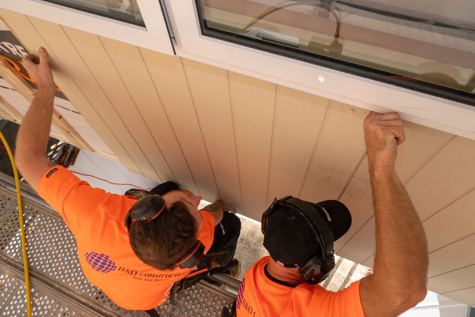 Two men in orange shirts are working on a window.