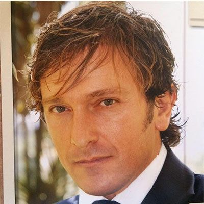 Ritratto ravvicinato di un uomo in abito scuro, che guarda in camera con un'espressione neutra.