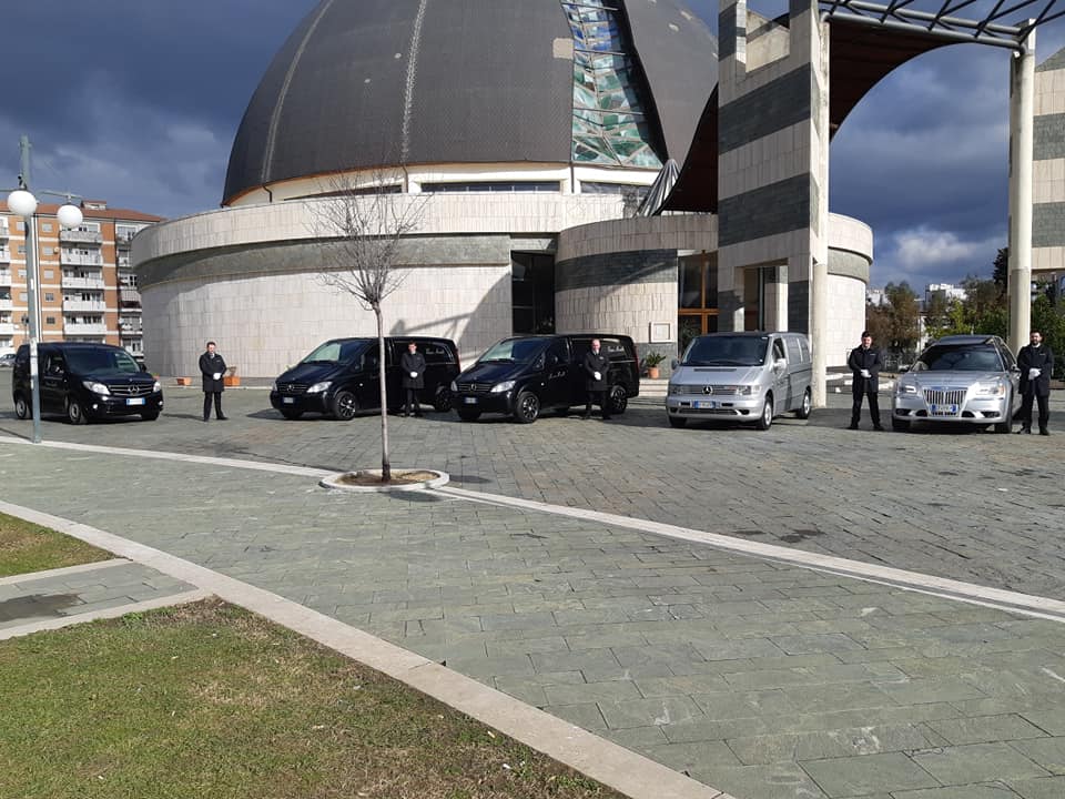 In una giornata di sole, un carro funebre Jaguar color argento era parcheggiato su una strada asfaltata di fronte alle case.