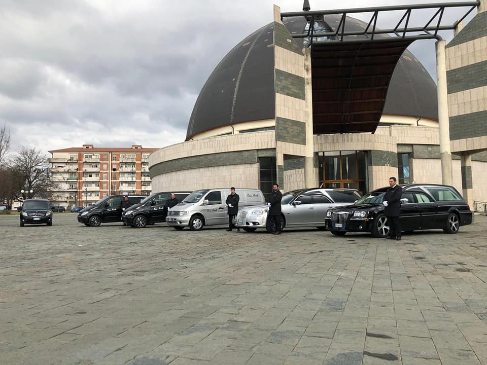In una giornata di sole, un carro funebre Jaguar color argento era parcheggiato su una strada asfaltata di fronte alle case.