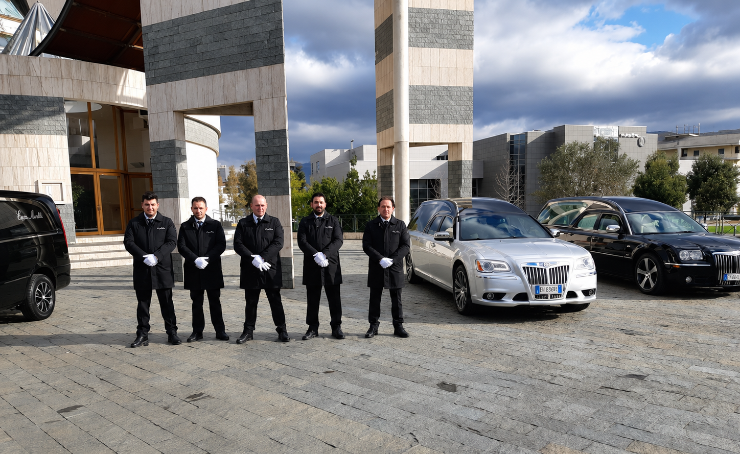 Cinque persone sono in piedi in un parcheggio accanto ad auto parcheggiate e a un edificio a strisce