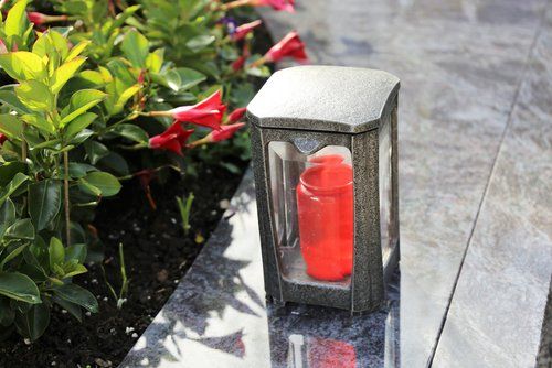 Candela rossa all'interno di una lanterna di vetro su un sentiero di pietra accanto a piante verdi e fiori rossi.