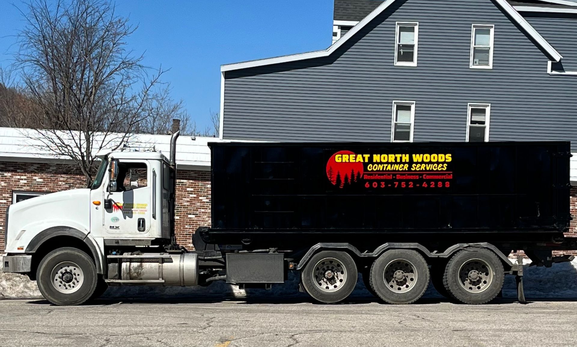 White truck with black dumpster parked in front of a building. The dumpster reads 