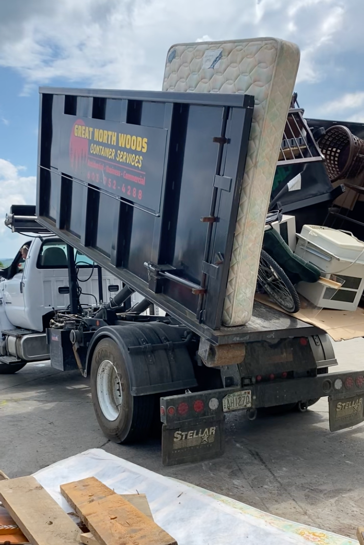 Dump truck with raised bed, hauling a mattress and scrap metal.