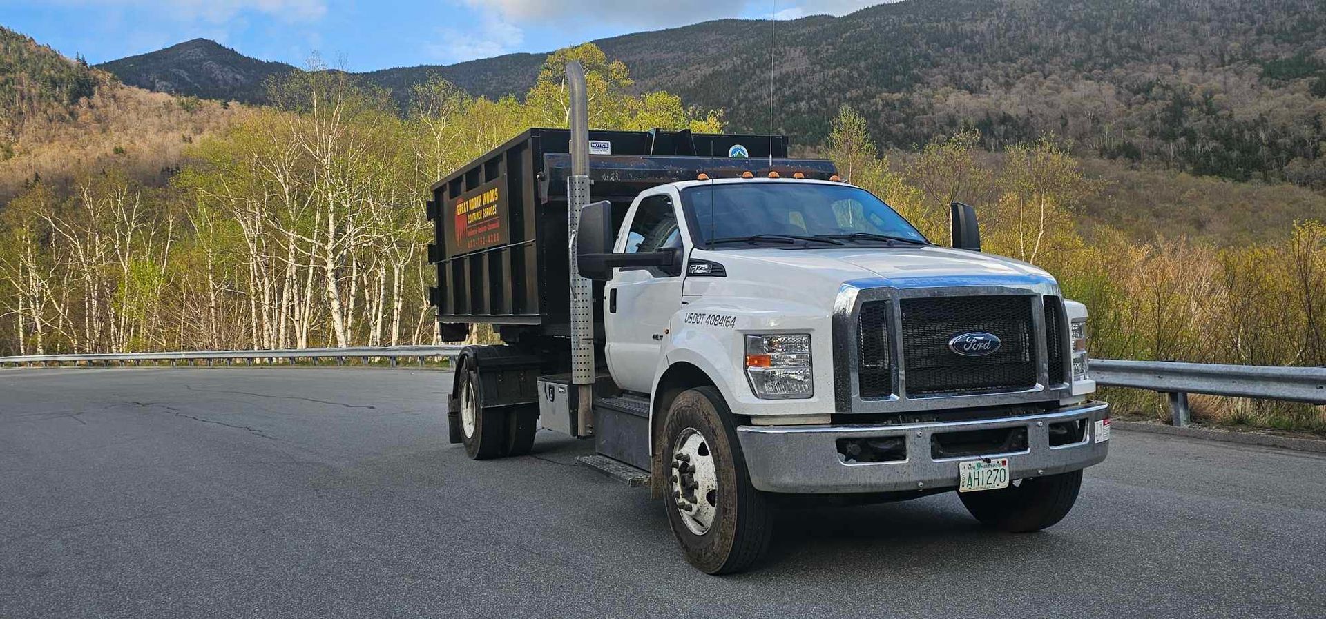 White dump truck on a road with mountains in the background.