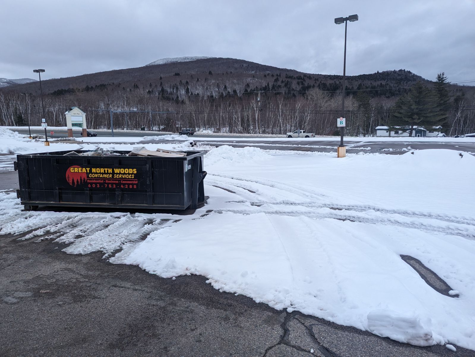 A commercial dumpster rental is sitting in the snow in a parking lot in Conway, NH.