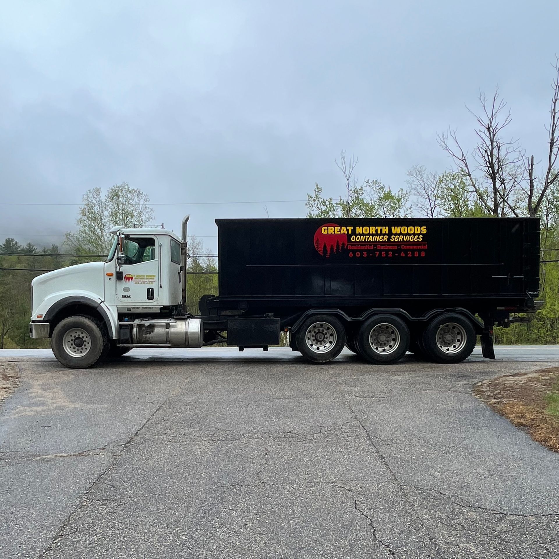 White dump truck on road, with a black dumpster. 