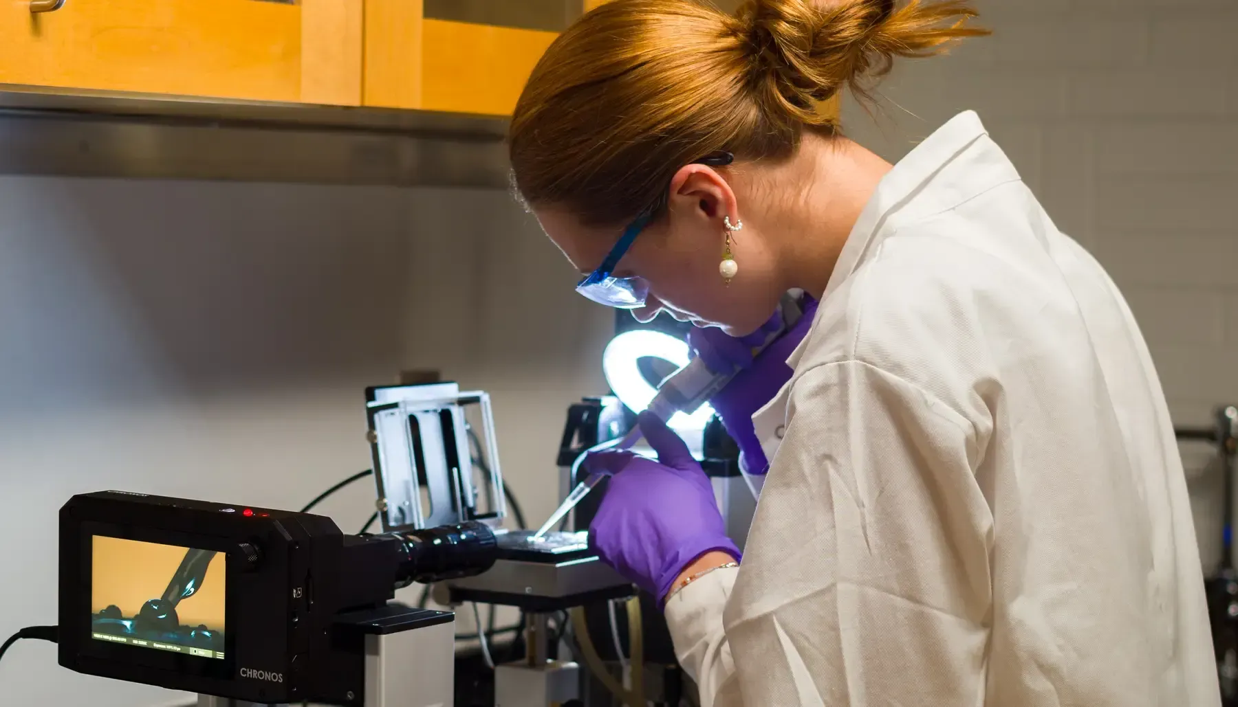 A woman in a lab coat is looking through a microscope.