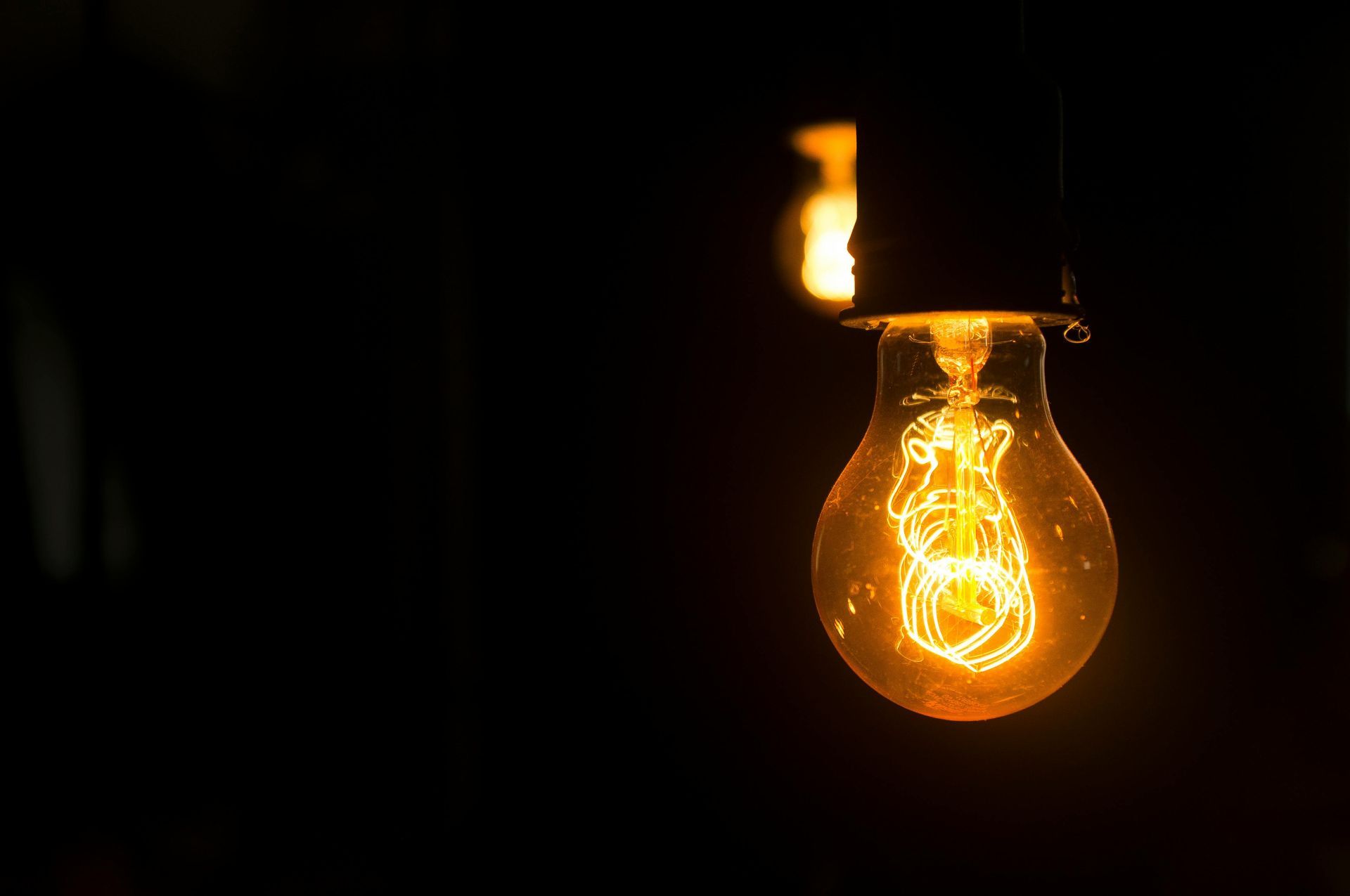 Lit lightbulb hanging in the dark, glowing with orange light.