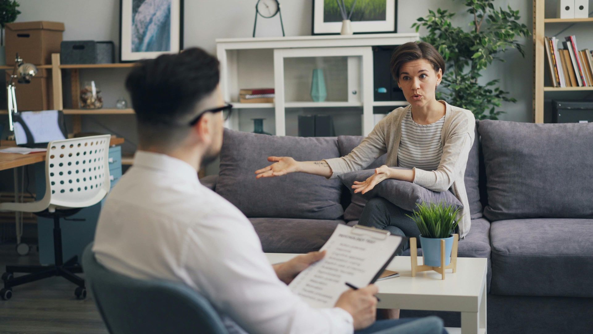 Woman talking to a therapist on a couch; therapist taking notes.
