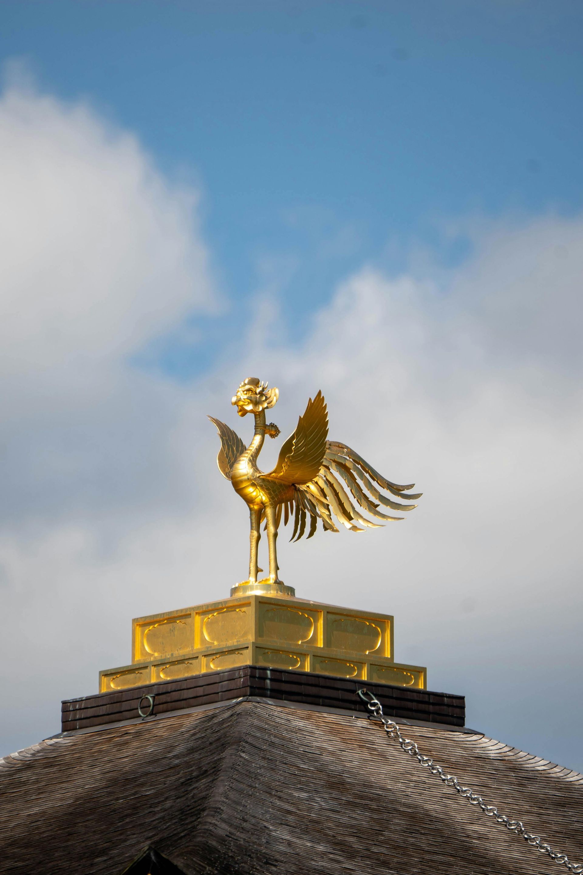 A golden bird is sitting on top of a thatched roof.