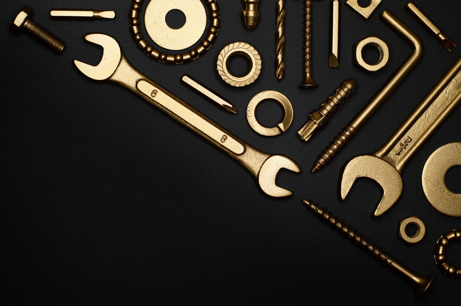 A collection of gold-colored tools and fasteners, including wrenches, washers, and screws, arranged on a black background.