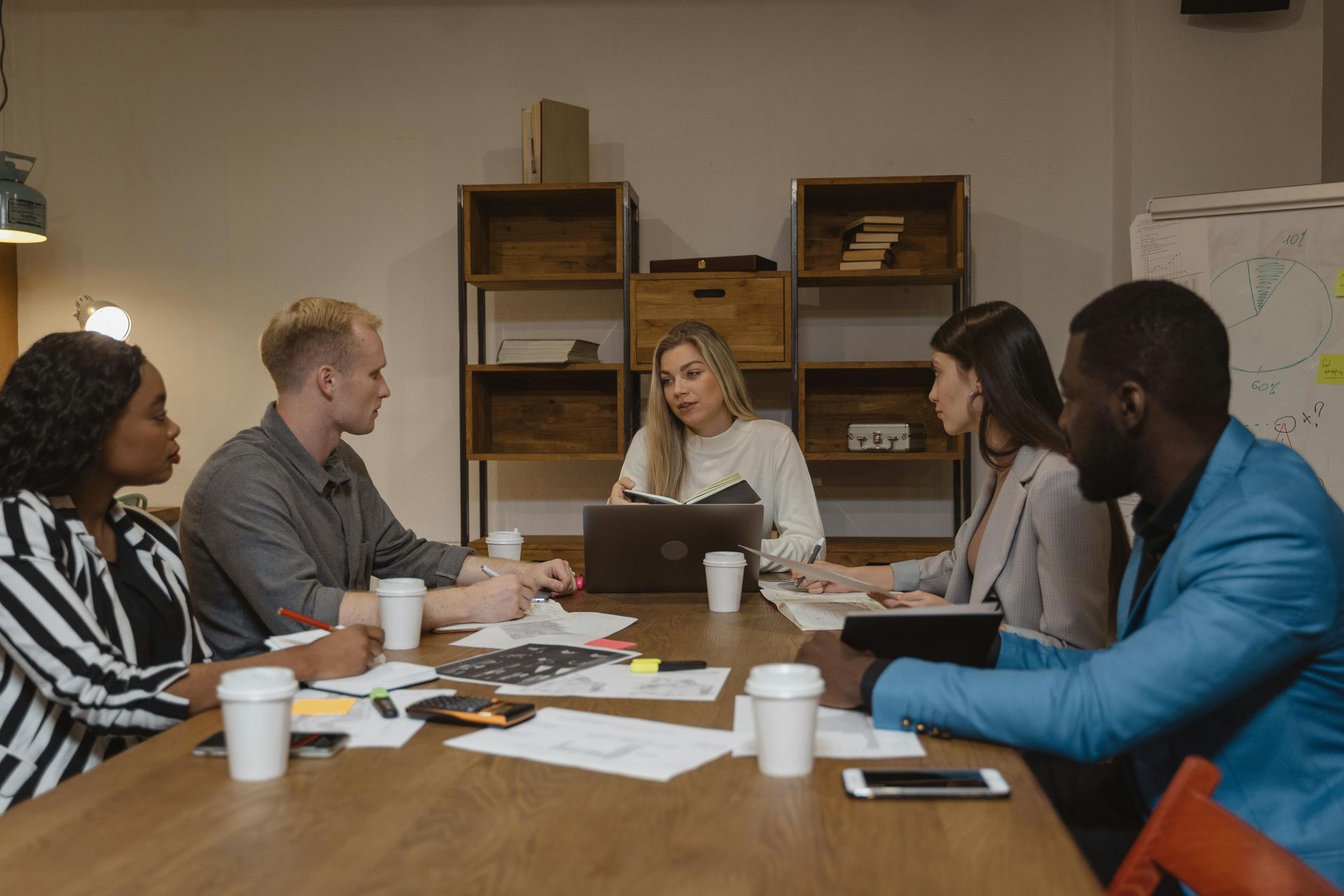 Group of people at a table, looking at documents and a laptop, in a dimly lit office.