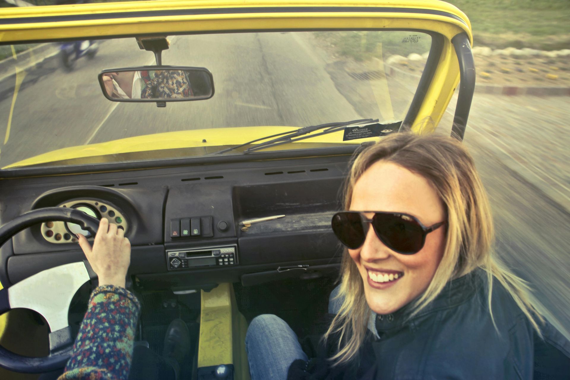 A woman wearing sunglasses is driving a yellow car.
