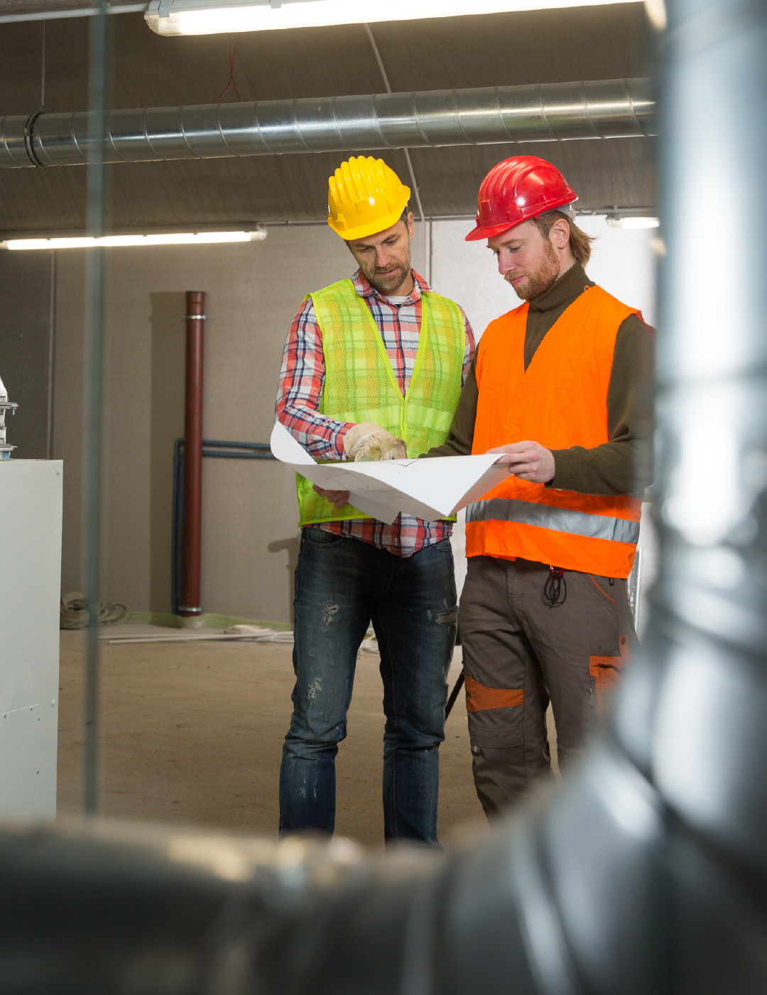 Two construction workers are looking at a blueprint in a building.