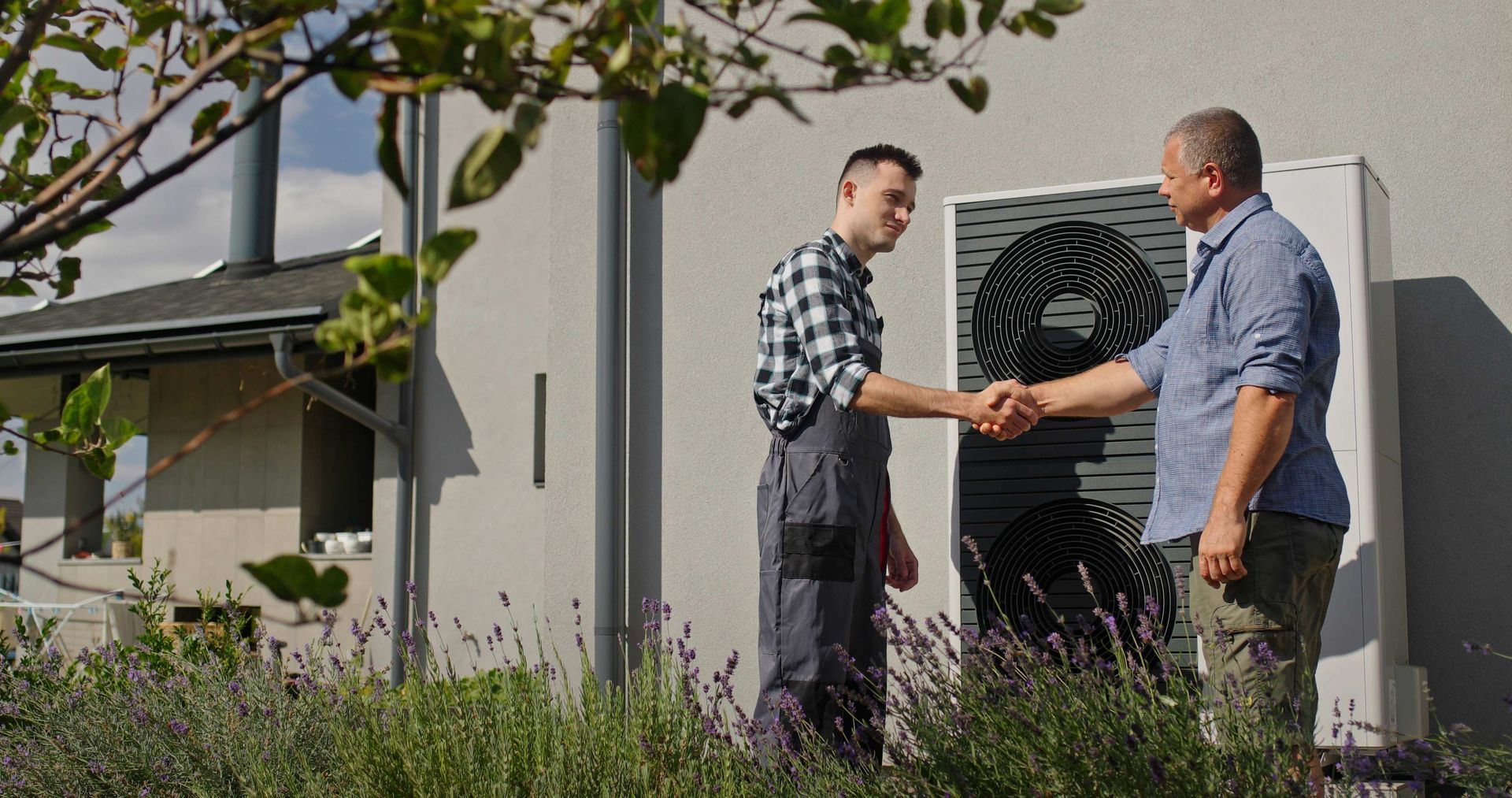 Two men shaking hands in front of a heat pump outside a house.