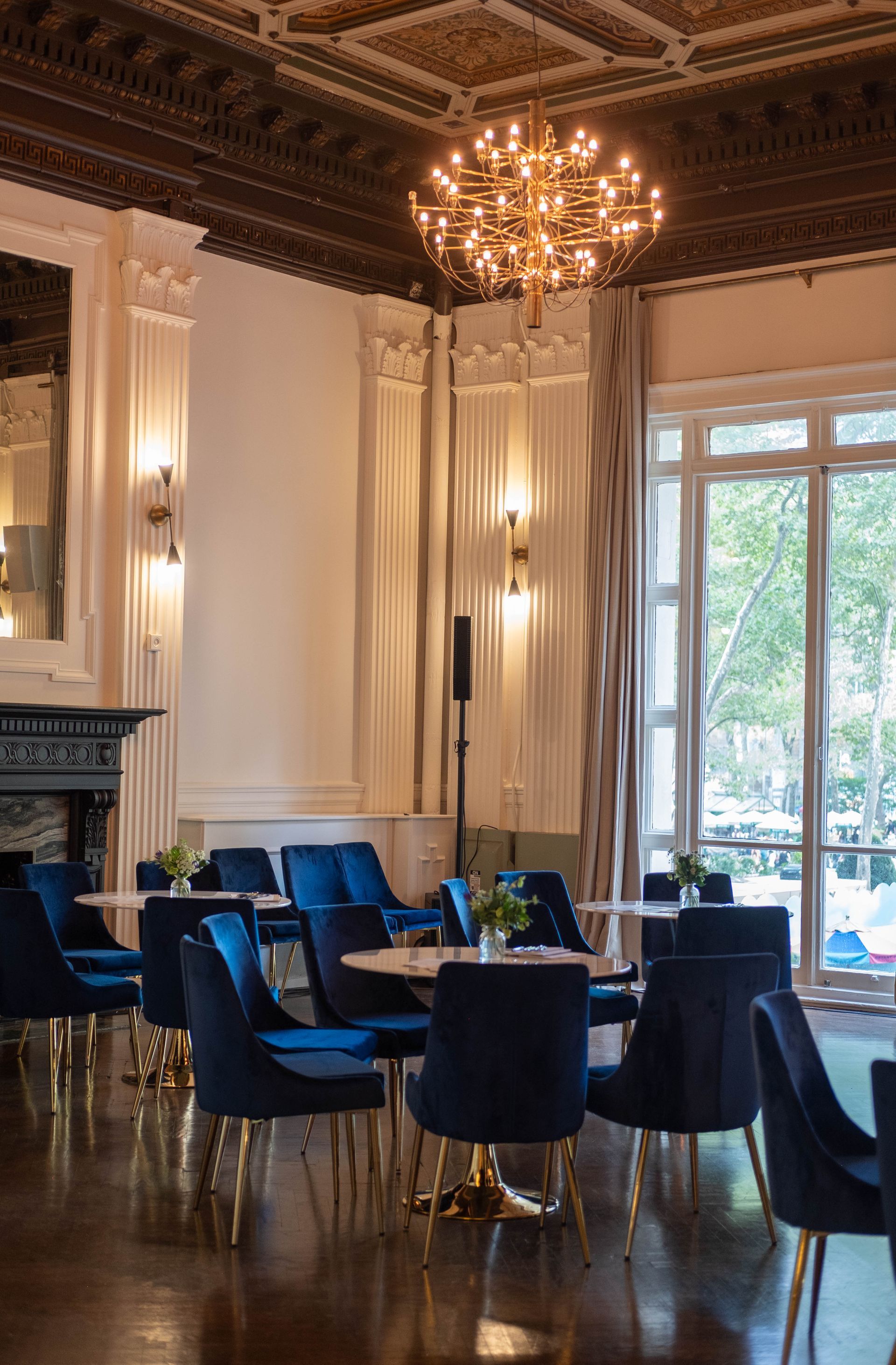 Elegant dining room with blue chairs, dark wood floors, chandeliers, and large windows overlooking trees