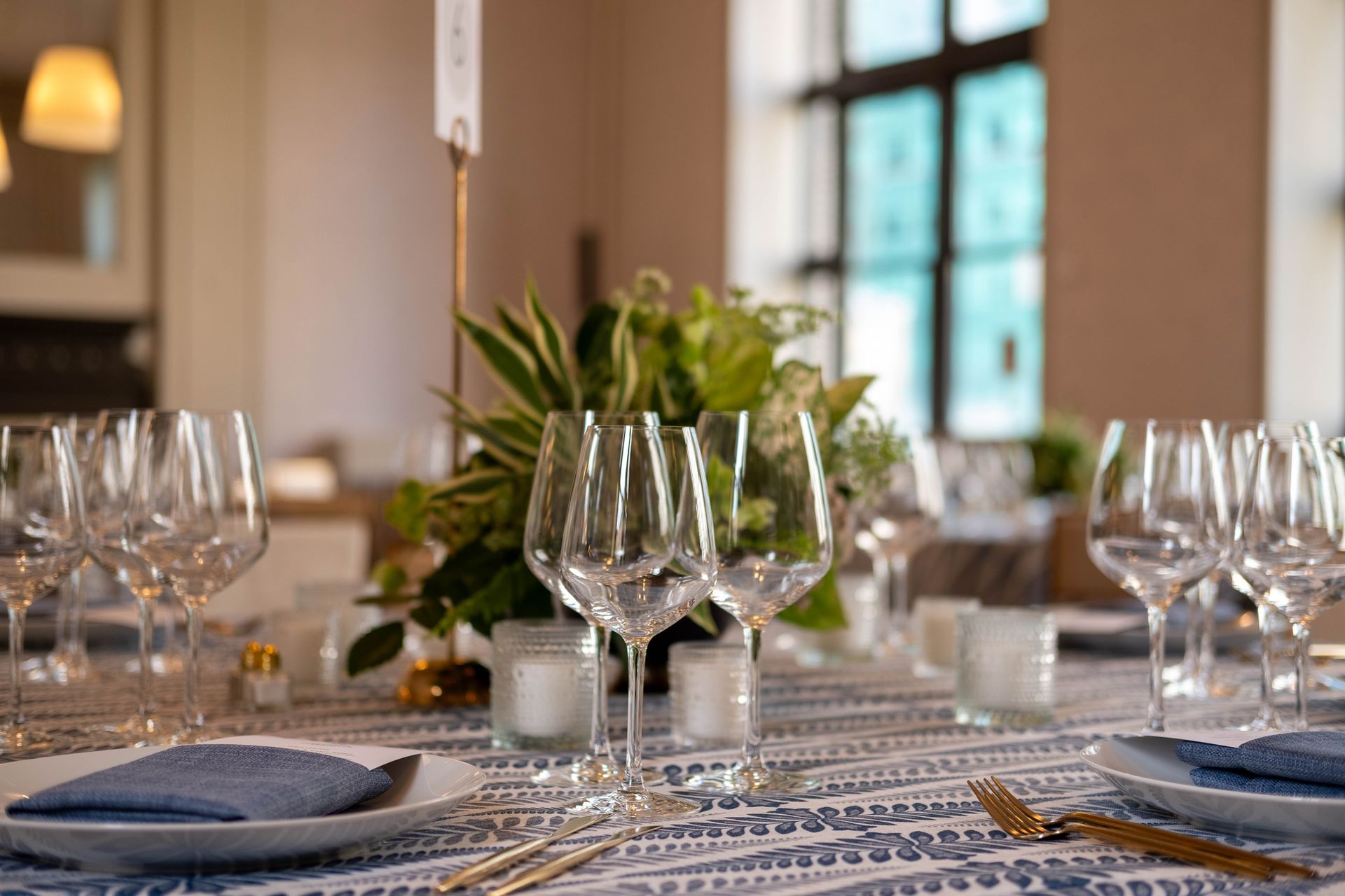 Set dining table with wine glasses, blue napkins, and a floral centerpiece in a bright room