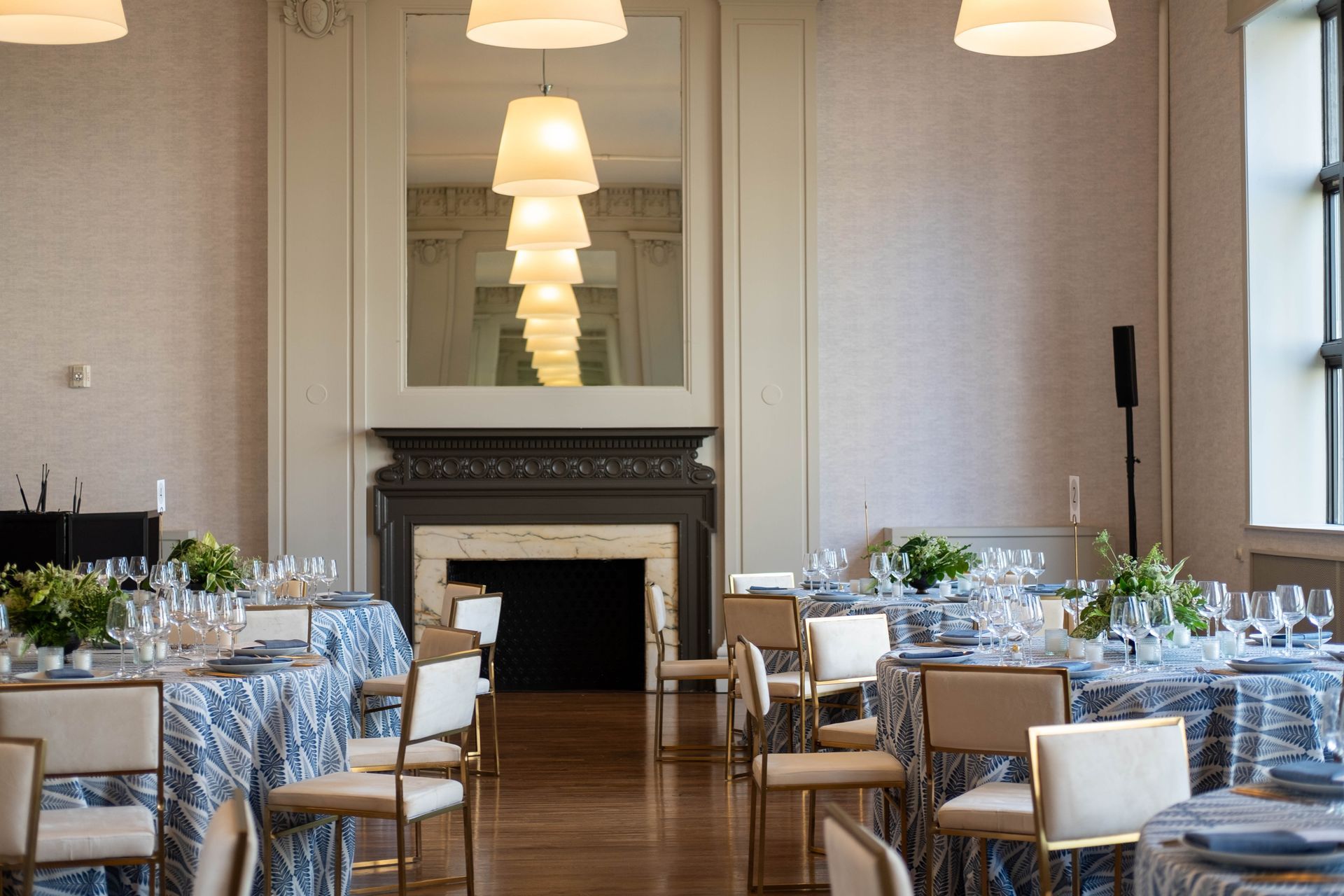 Elegant dining room with set tables, blue floral chairs, and a fireplace with mirrored mantel