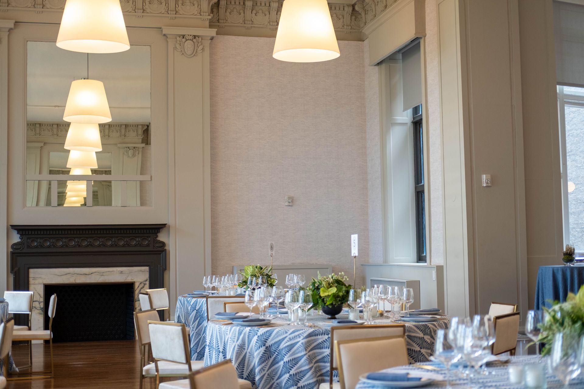 Elegant dining room with set tables, pendant lights, a fireplace, and large mirror.
