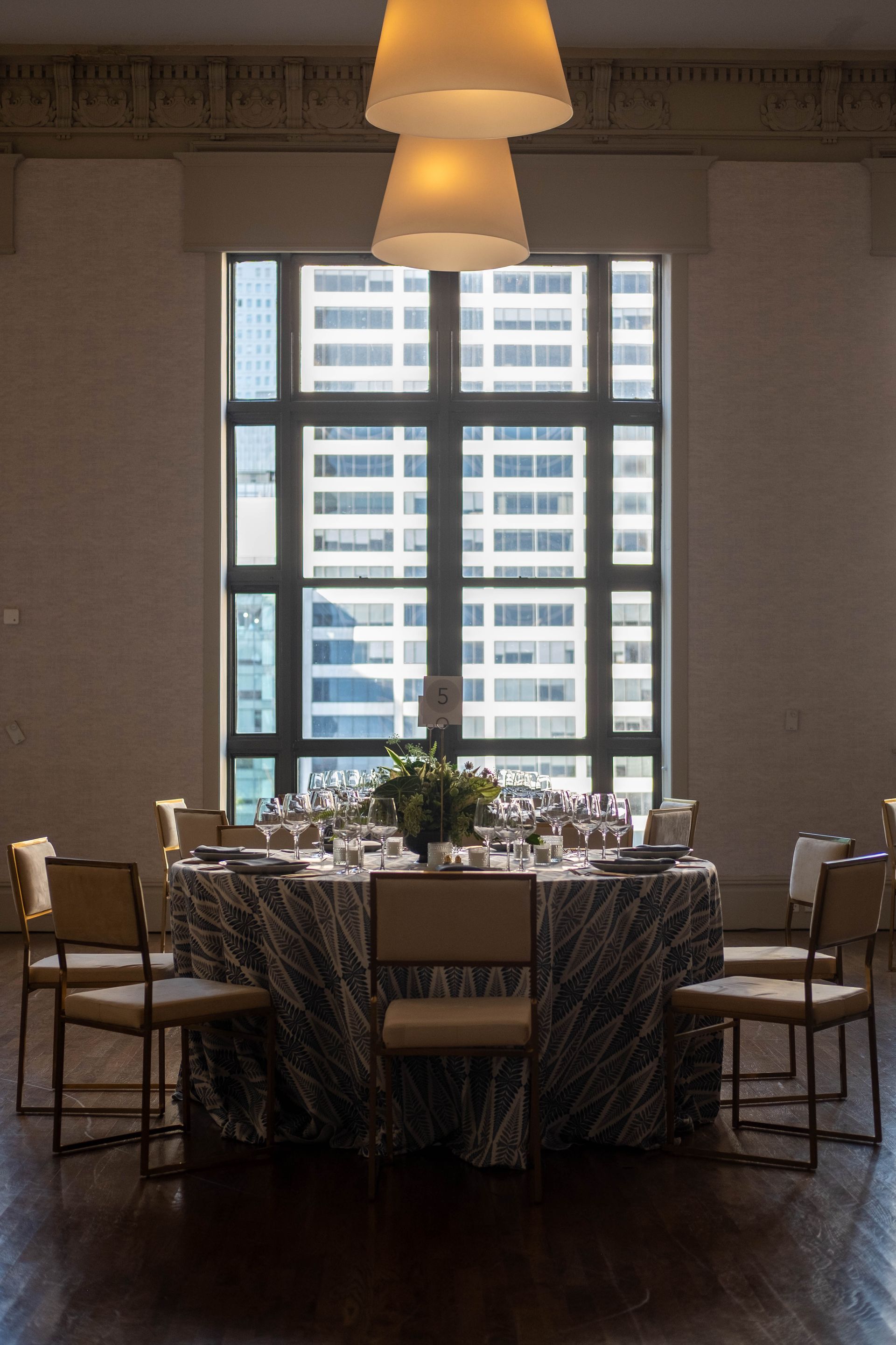Dining table set for a meeting in a softly lit room with a large window and city view.