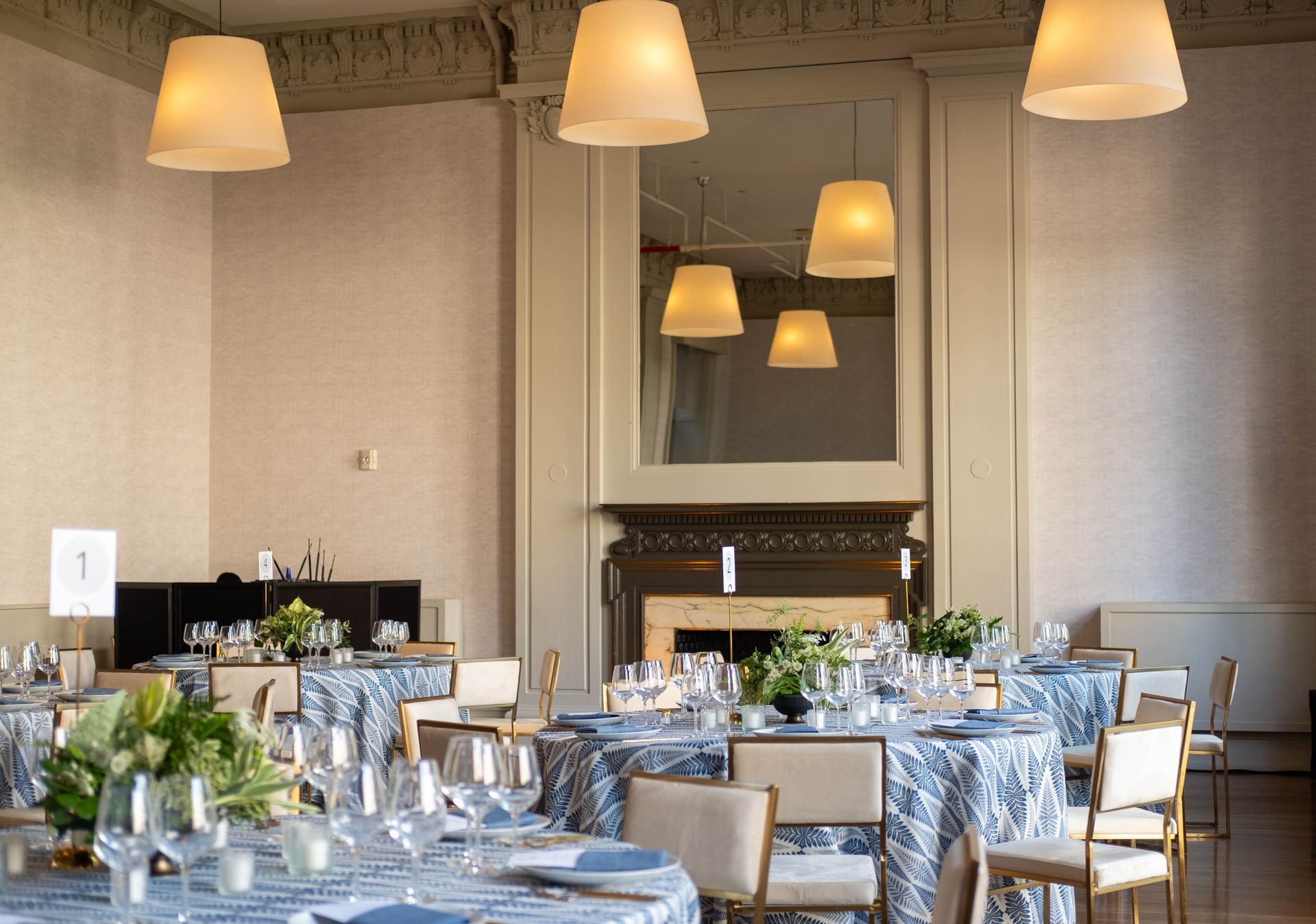Elegant dining room with set tables, upholstered chairs, and warm pendant lights near a fireplace