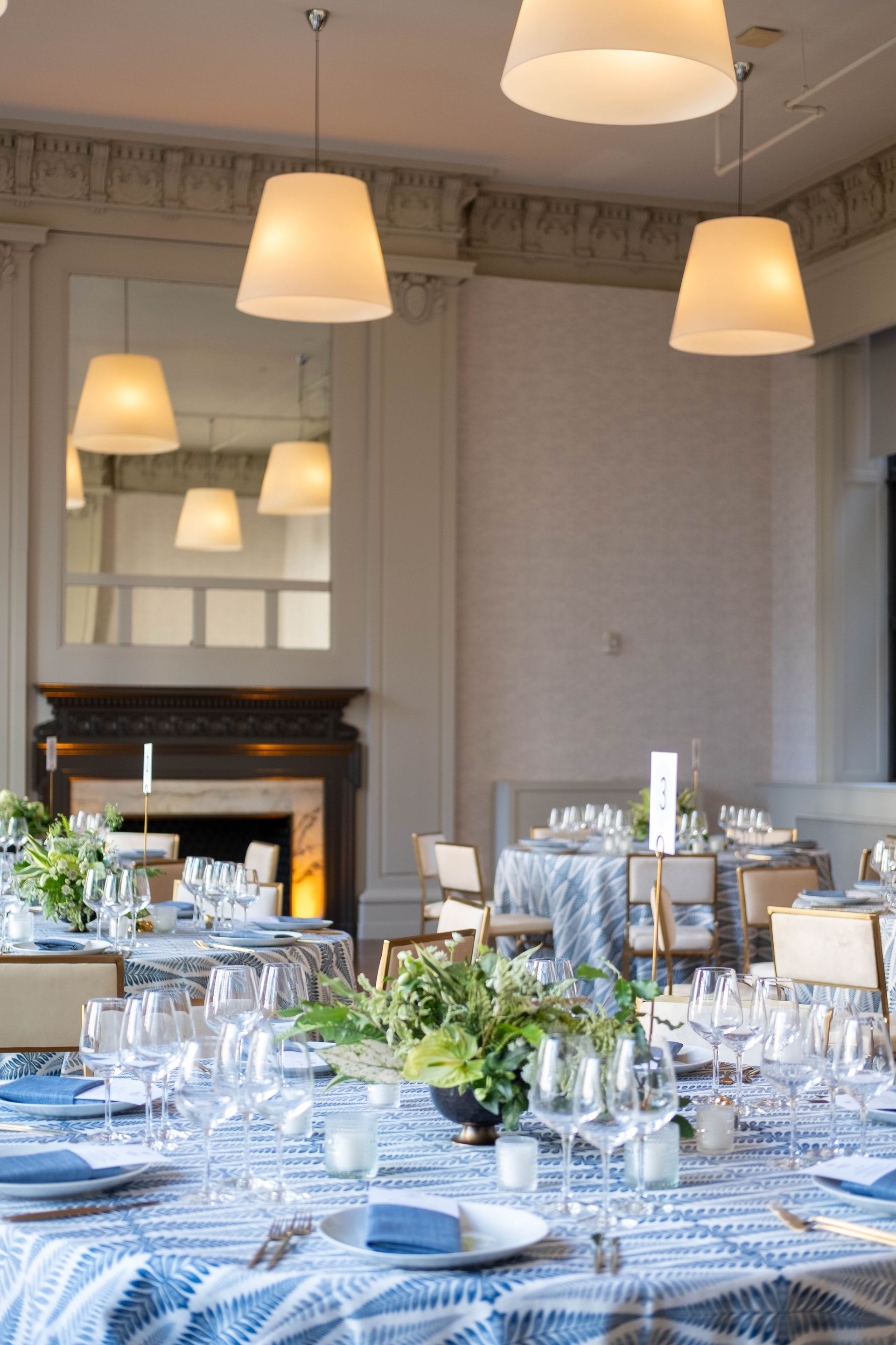 Elegant dining room with a set table, blue checkered cloth, hanging lamps, and a fireplace
