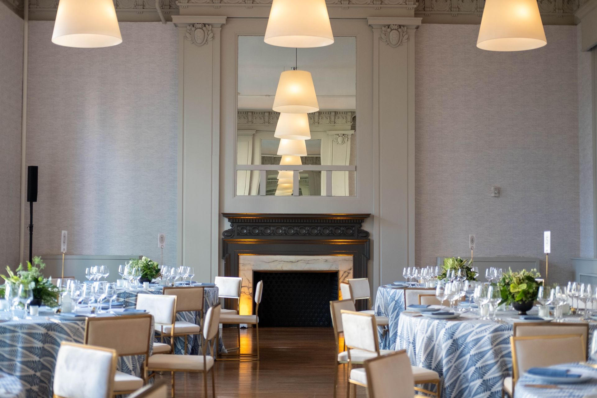Elegant dining room with set tables, hanging lamps, and a fireplace centered on the far wall