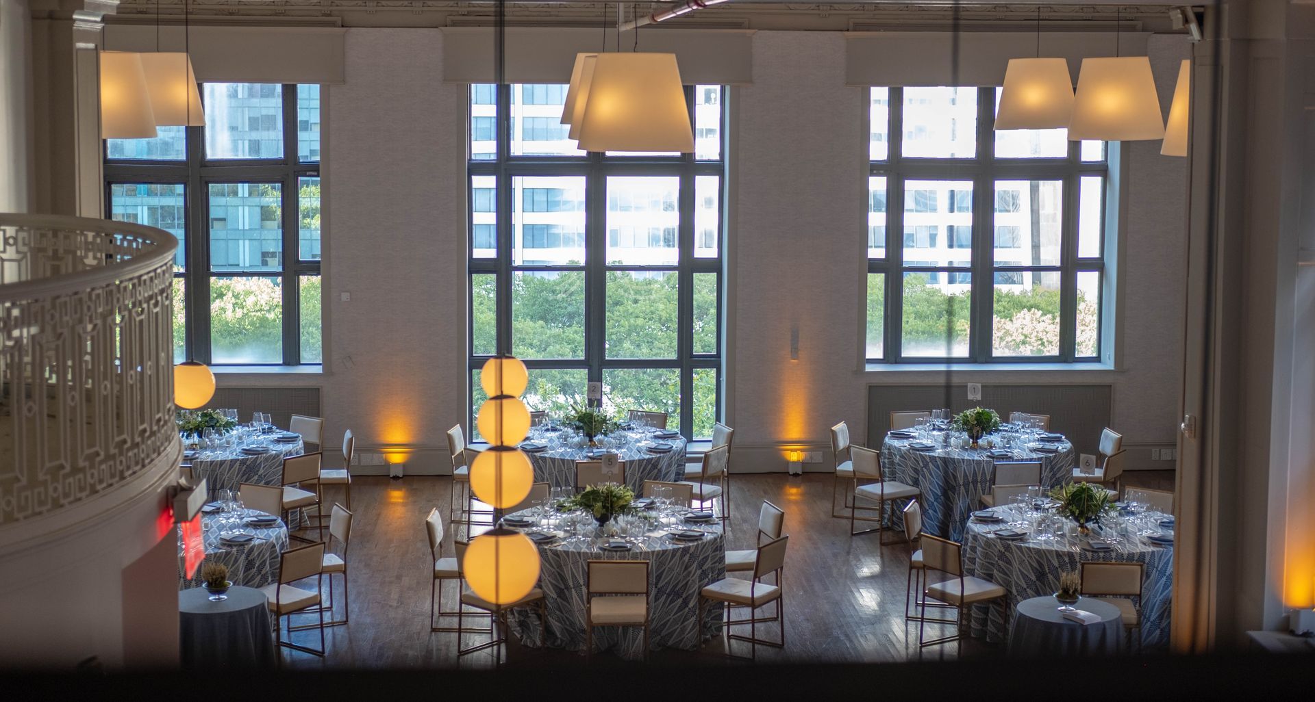Elegant restaurant dining room with set tables, warm pendant lights, and large windows overlooking greenery