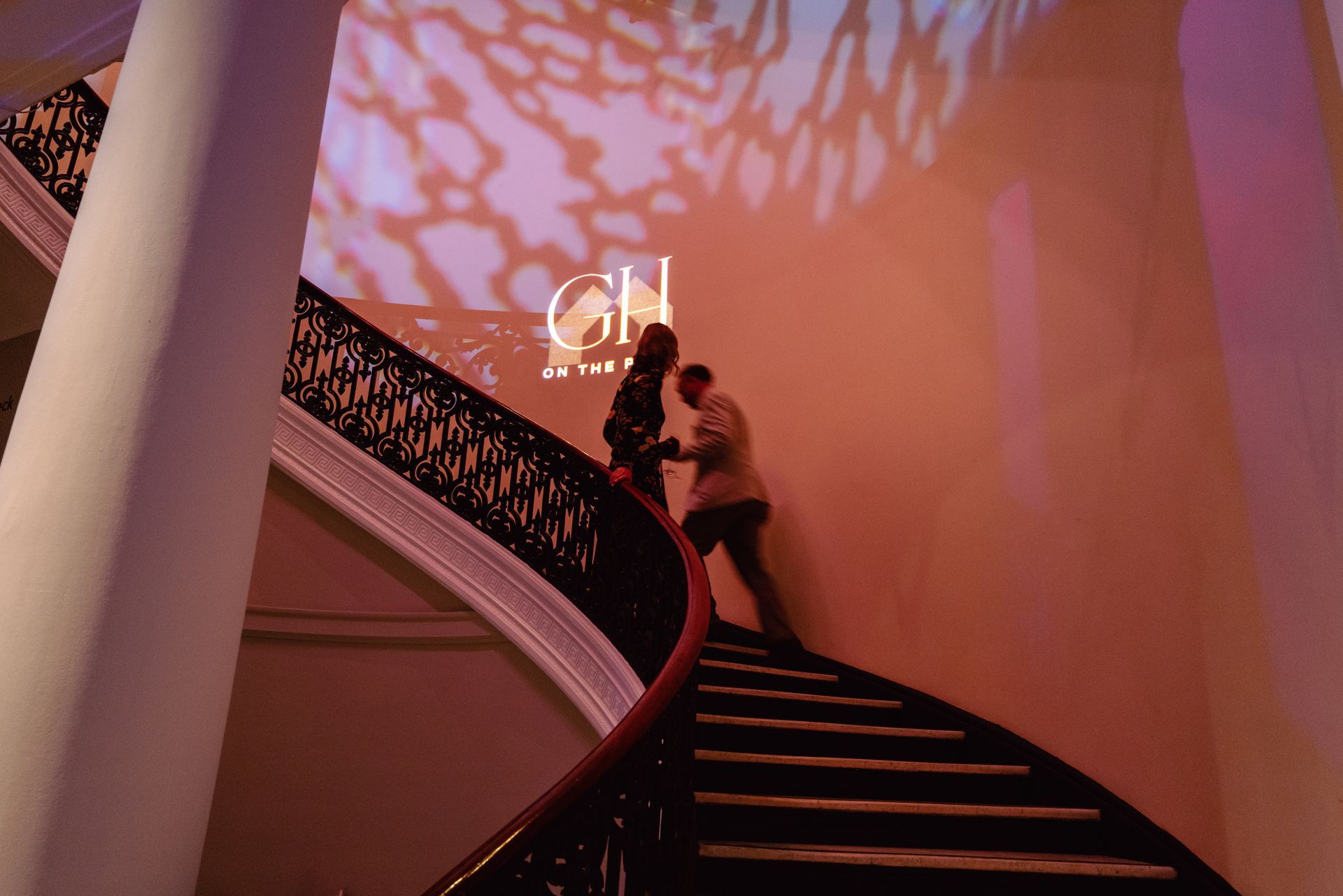 Two people on a curved staircase under pink lighting and patterned shadows