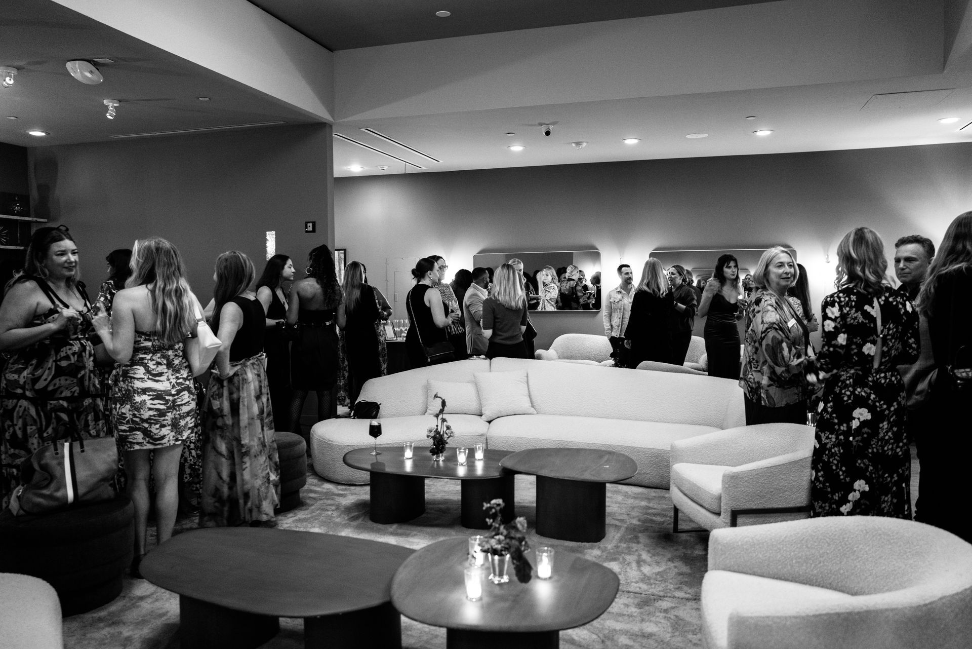 Guests mingle in a lounge with curved sofas and cocktail tables during a social event.