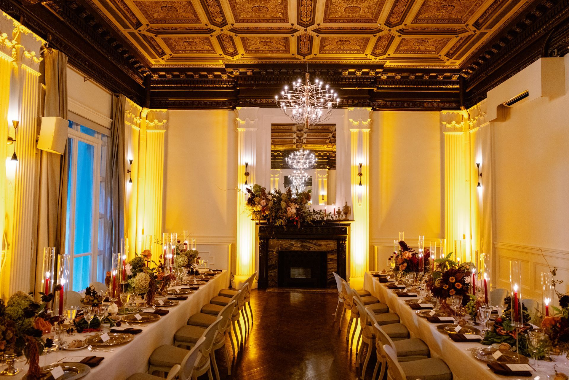 Elegant banquet hall with long tables, chandeliers, gold ceiling, and warm lighting