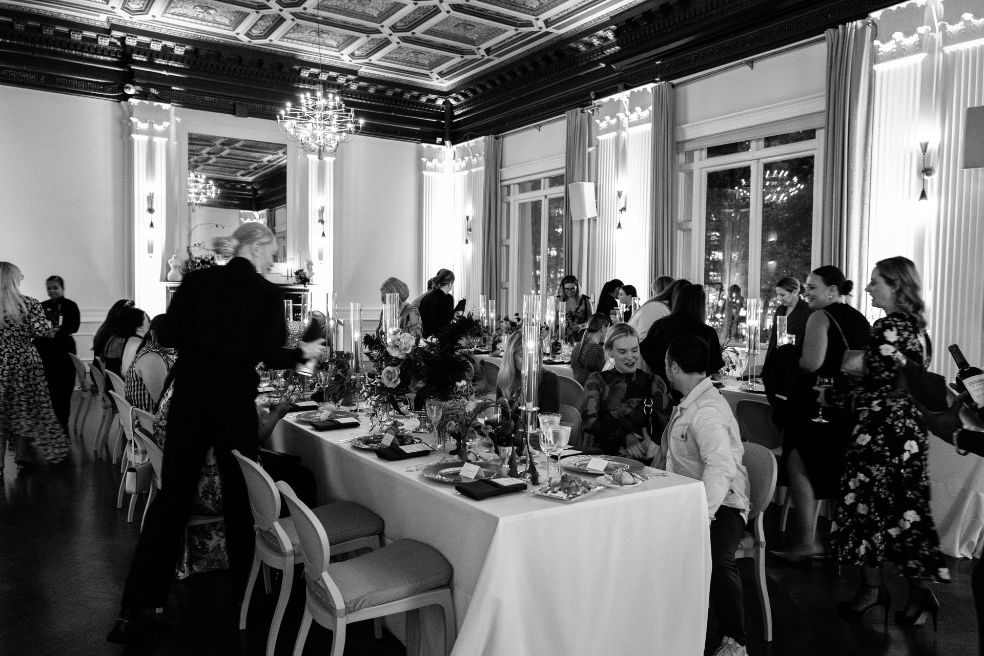 Guests seated around a formal banquet table in an ornate black-and-white dining room.