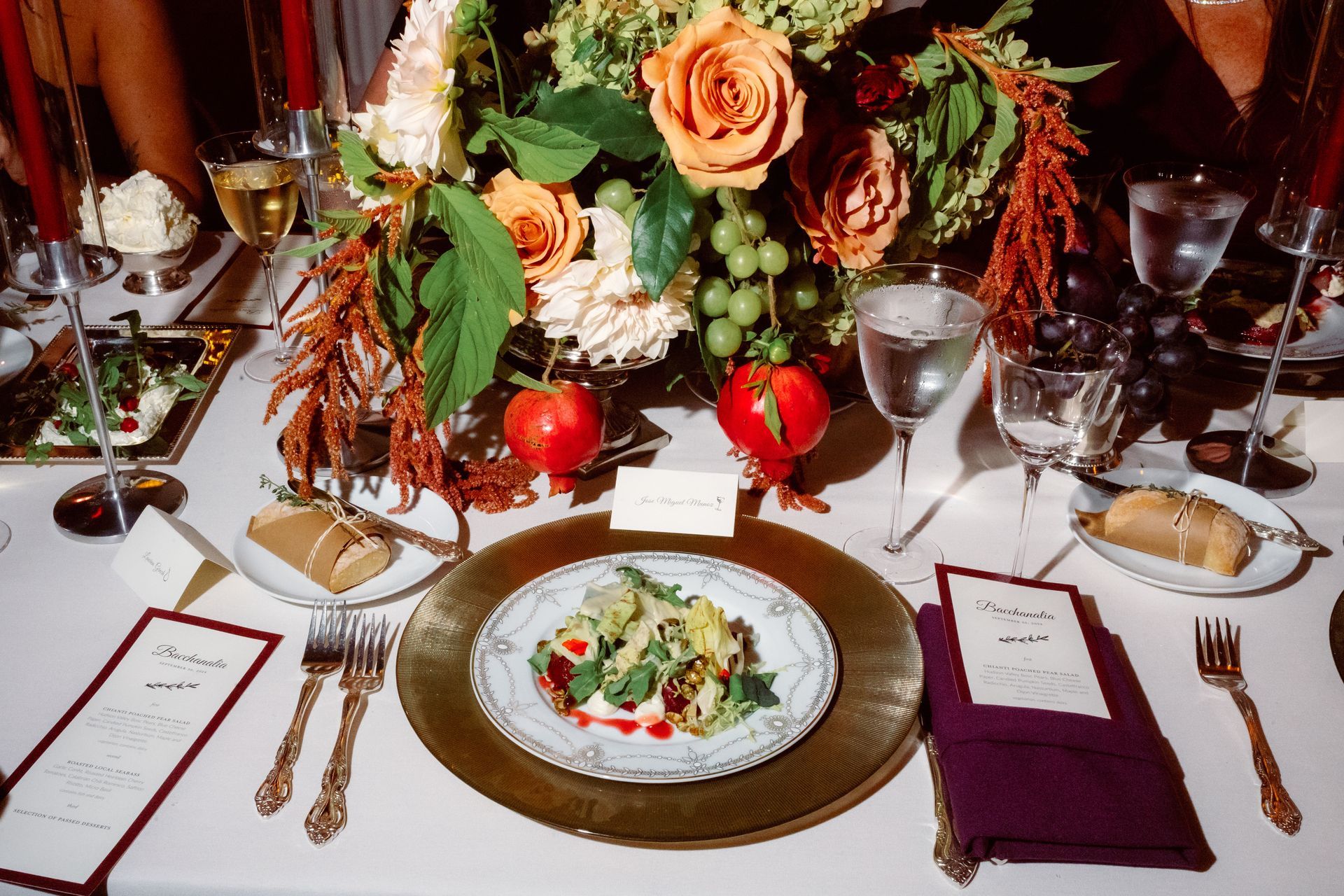 Elegant dining table set with salad, wine glasses, red roses, and burgundy napkins