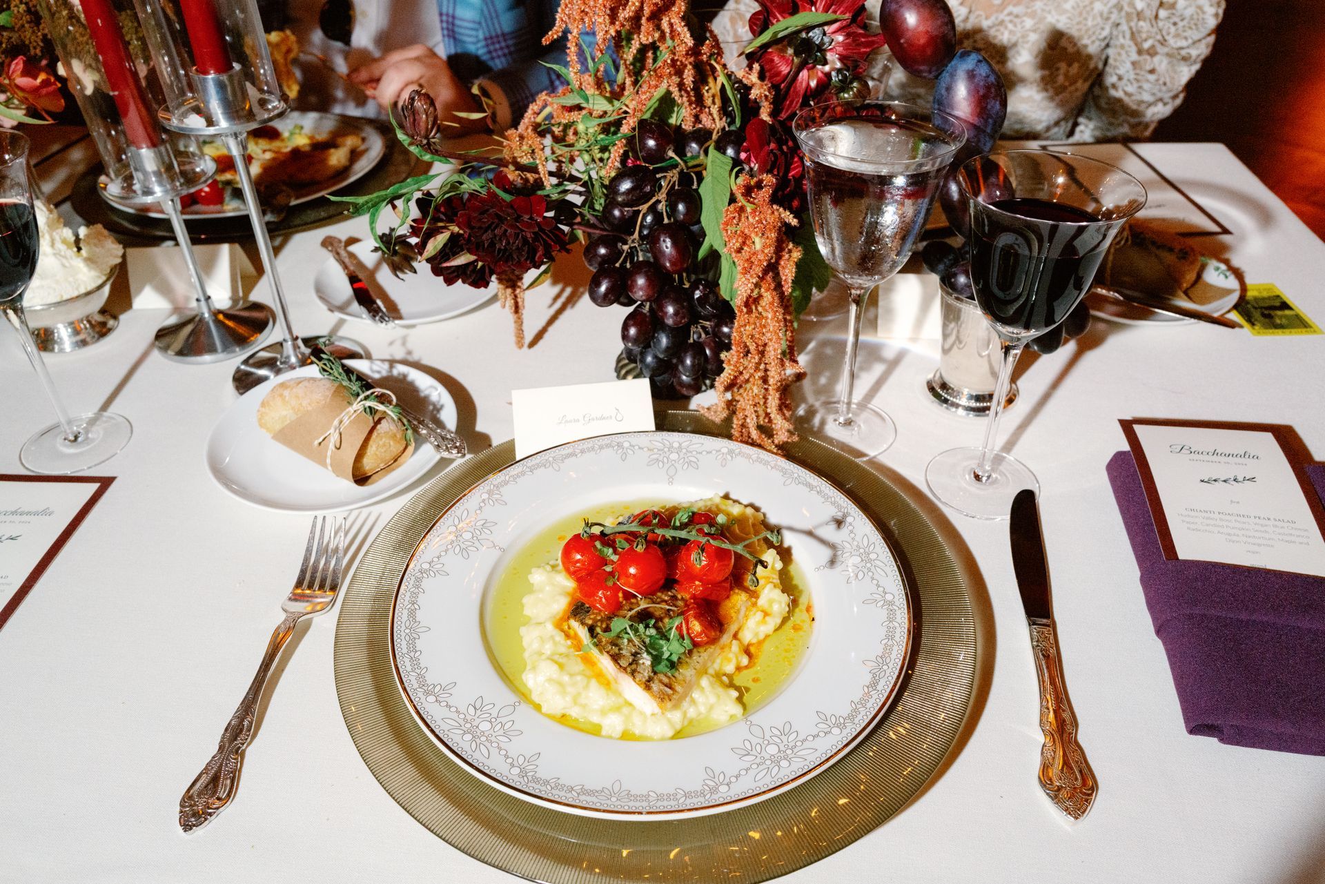 Formal dinner table with plated entrée, wine glasses, bread, and floral centerpiece
