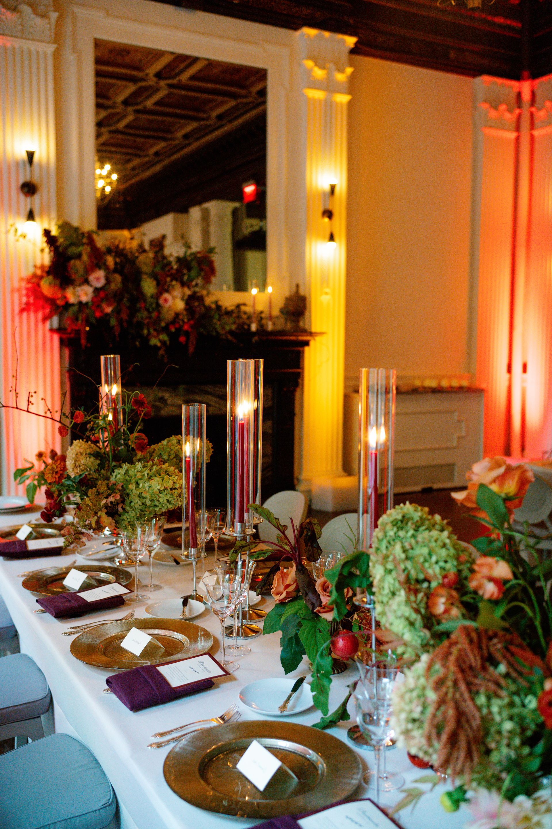 Elegant banquet table set with floral arrangements and candle centerpiece in a warmly lit hall