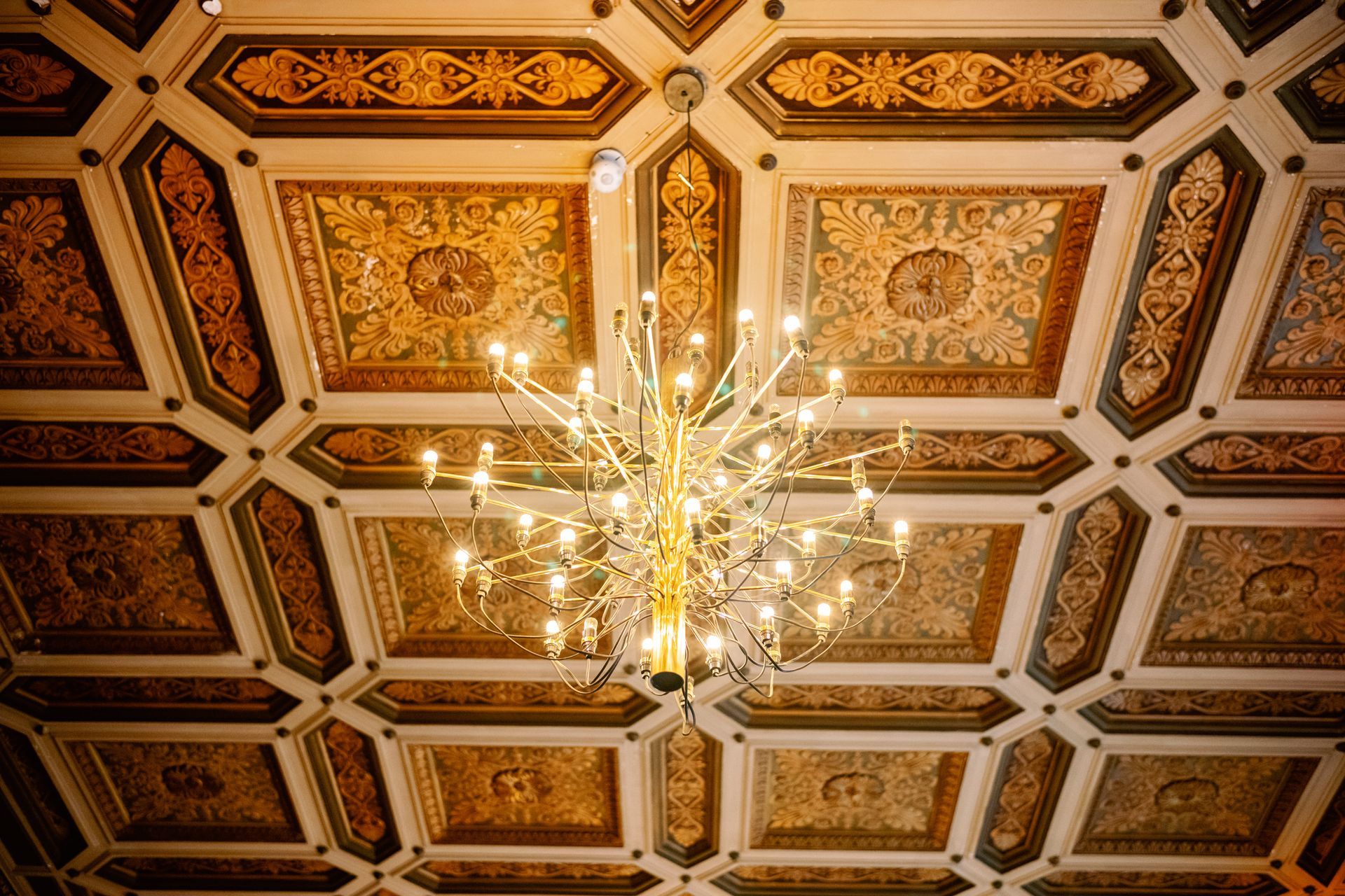 Ornate coffered ceiling with gold detailing and a central chandelier