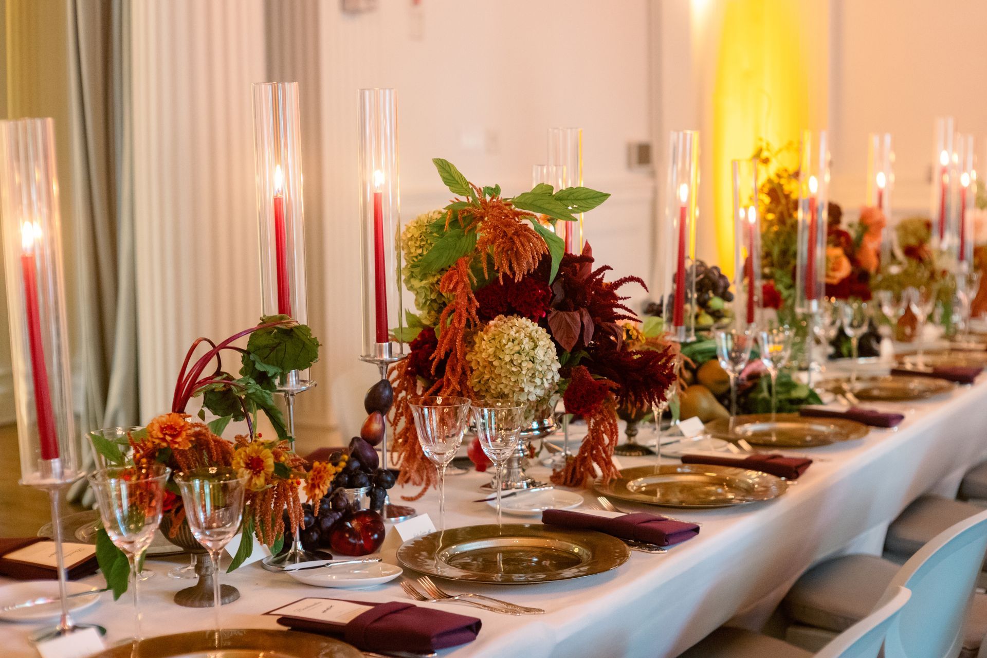 Elegant dining table set with red candles, autumn floral centerpiece, and glassware in a warm-lit room