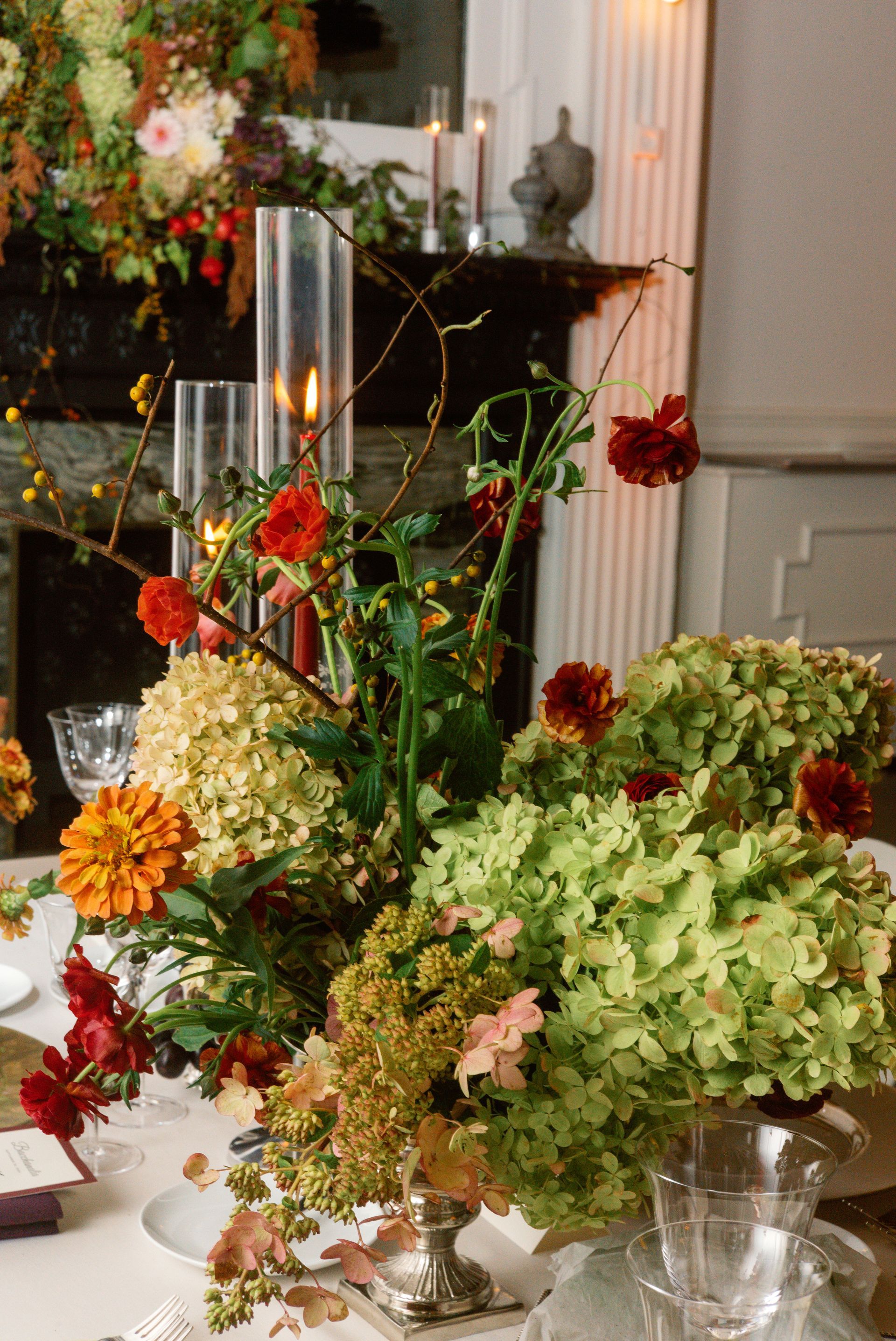Elegant floral arrangement with red, orange, and green blooms on a candlelit dining table